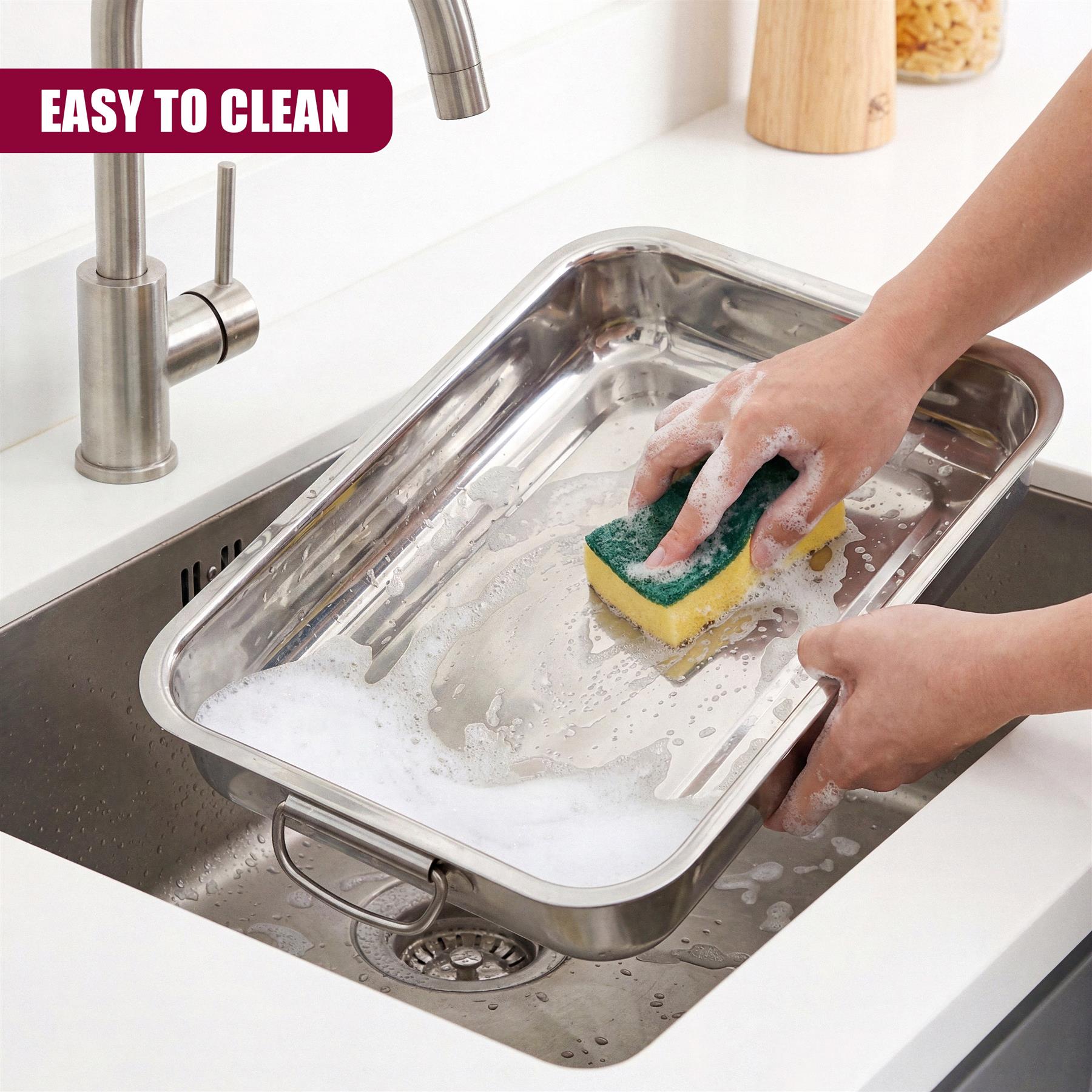 Soapy sponge cleans a stainless steel roasting tray placed in a sink.
