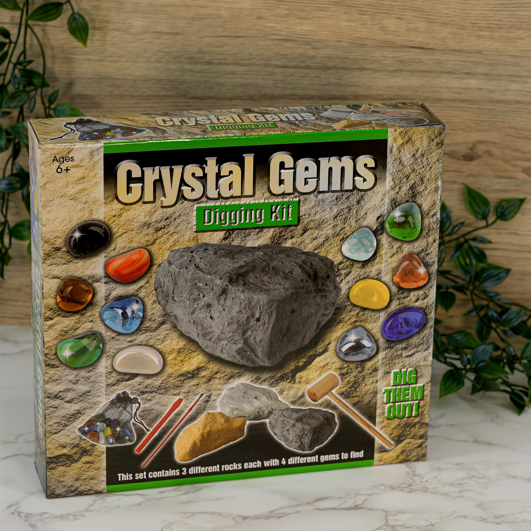 Product box containing colored faux gems, small tools, and three gray rocks for digging.