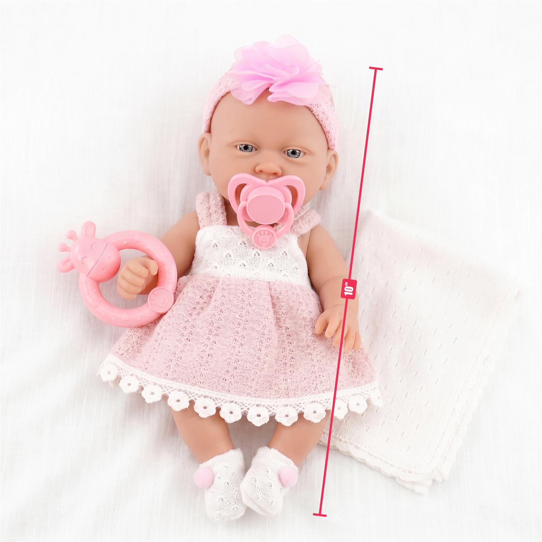 Doll wearing a pink lace dress, headband, and pacifier rests next to a pink rattle toy.