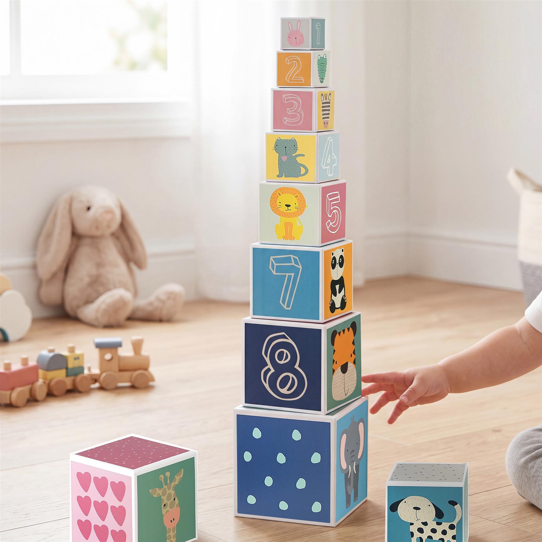 A towering stack of numbered, animal-themed blocks and several loose cubes rest on a wooden floor.