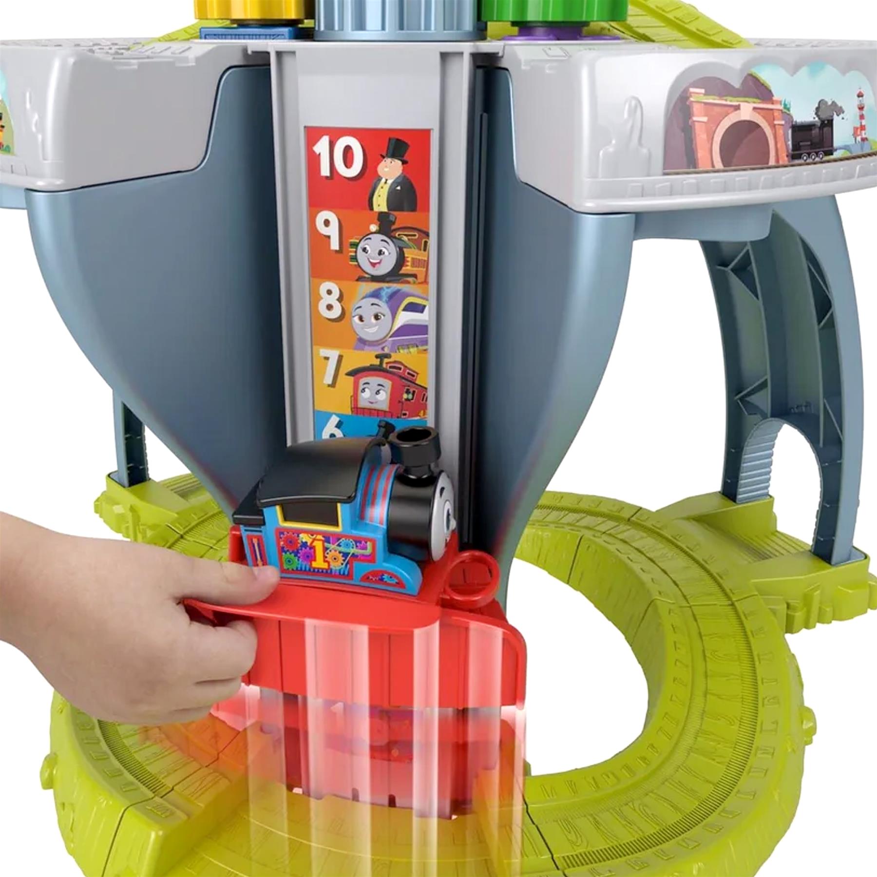 Child's hand pushing a blue train on a green track below a numbered learning toy table.