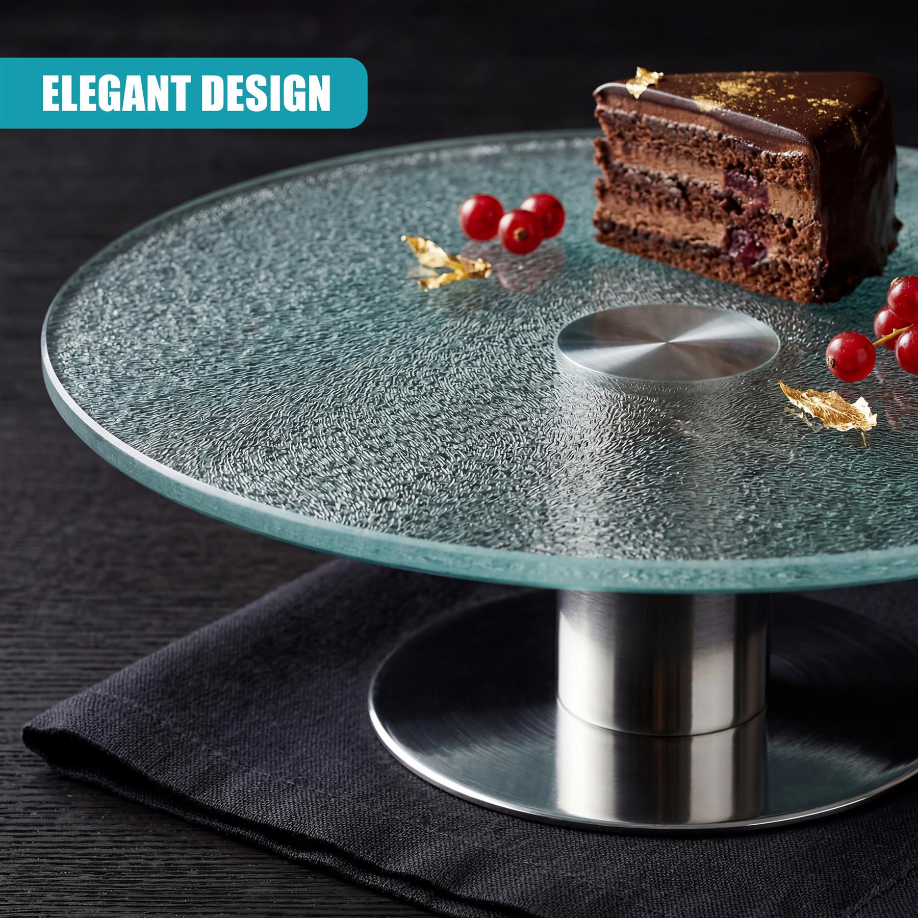 Round, glass cake stand on a metal pedestal, displaying a slice of cake, red berries, and scattered dried leaves.