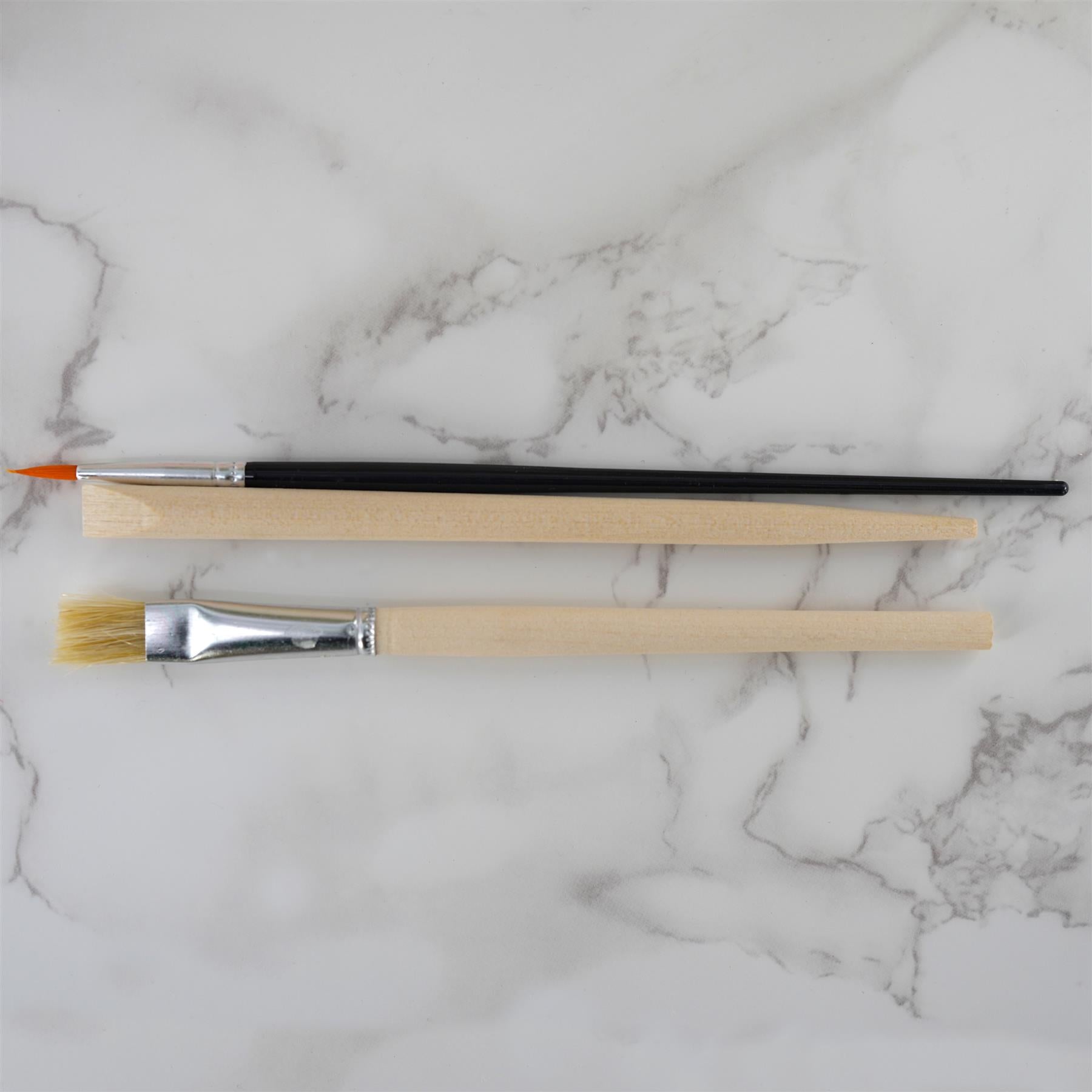 Three crafting tools—a paintbrush and two pointed excavation pointers—lay on white marble.
