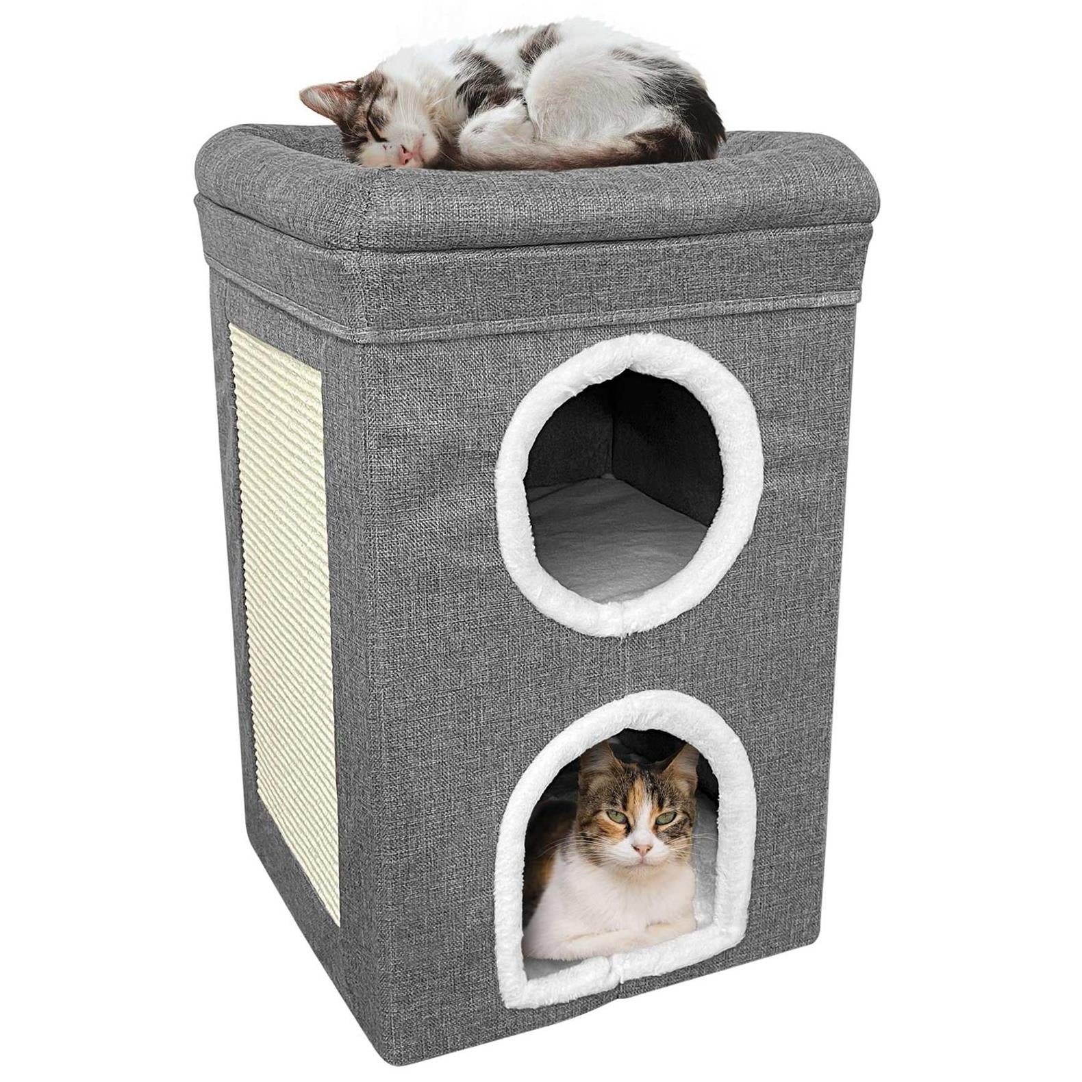 A cat sleeping on top of a two-story cat house with a grey, textured exterior and a white, plush interior. The house features two round windows with white, fluffy trim, and a cat is visible in the lower window, looking directly at the camera. - The Magic Toy Shop