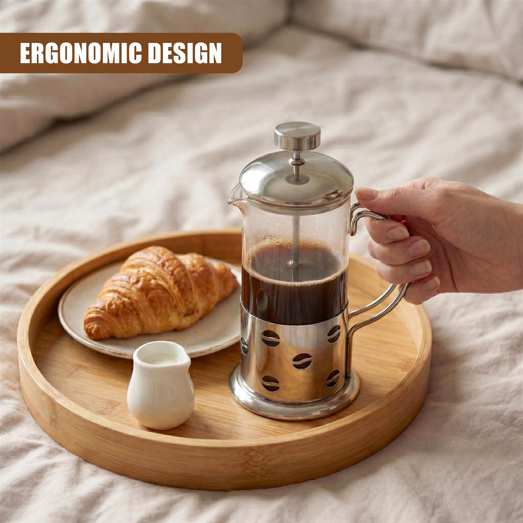 Metal cafetière filled with coffee rests on a wooden tray with a croissant and creamer.