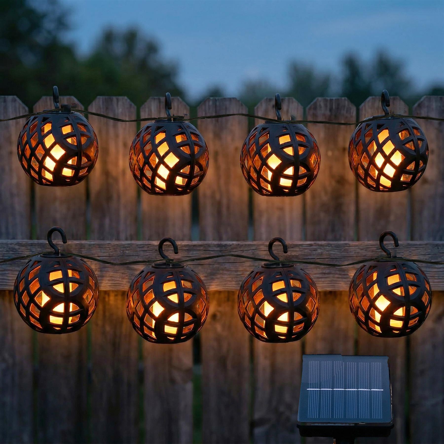 A string of woven rattan solar lights is draped across a rustic wooden fence.