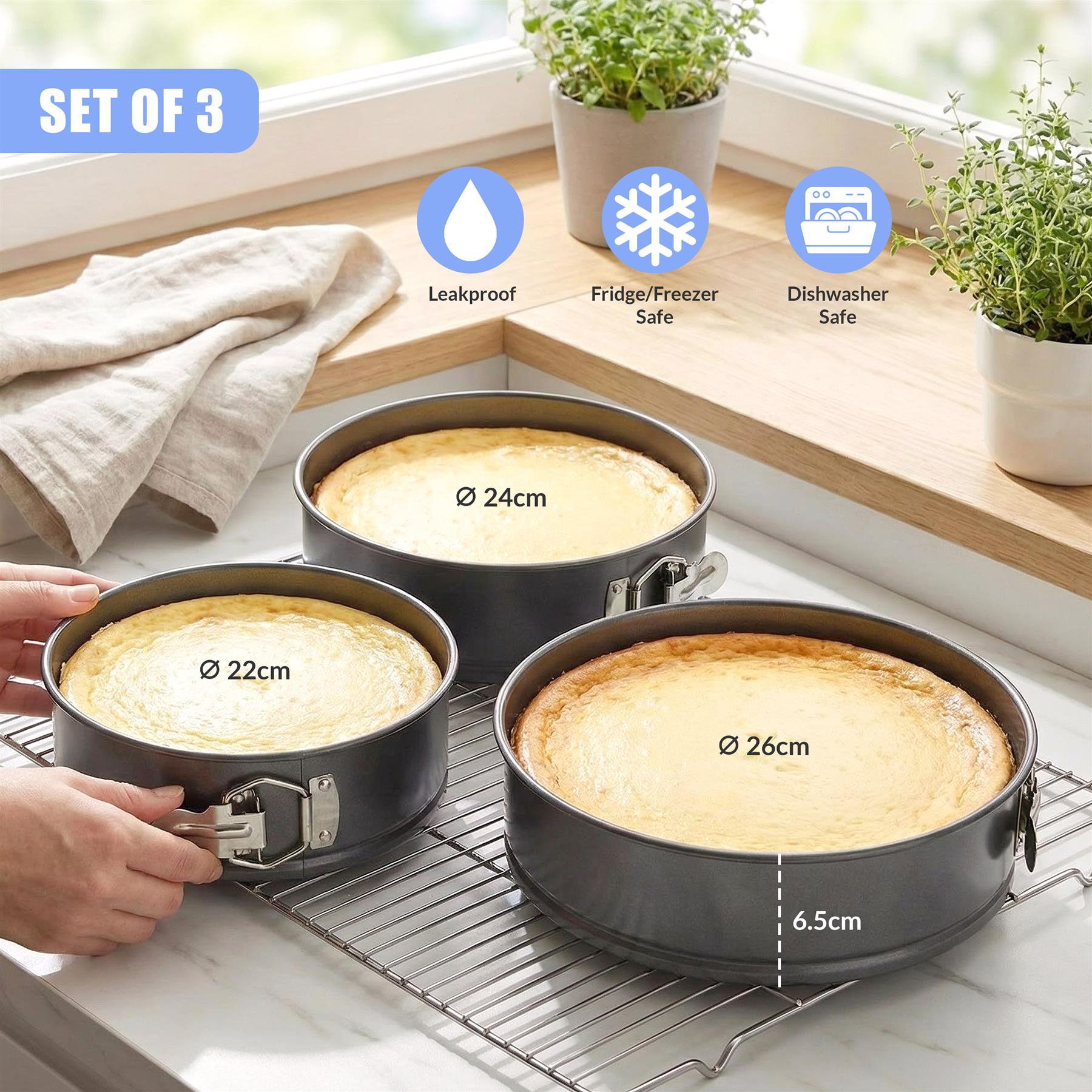 Three different sized, black springform cake pans are displayed on a wire cooling rack.