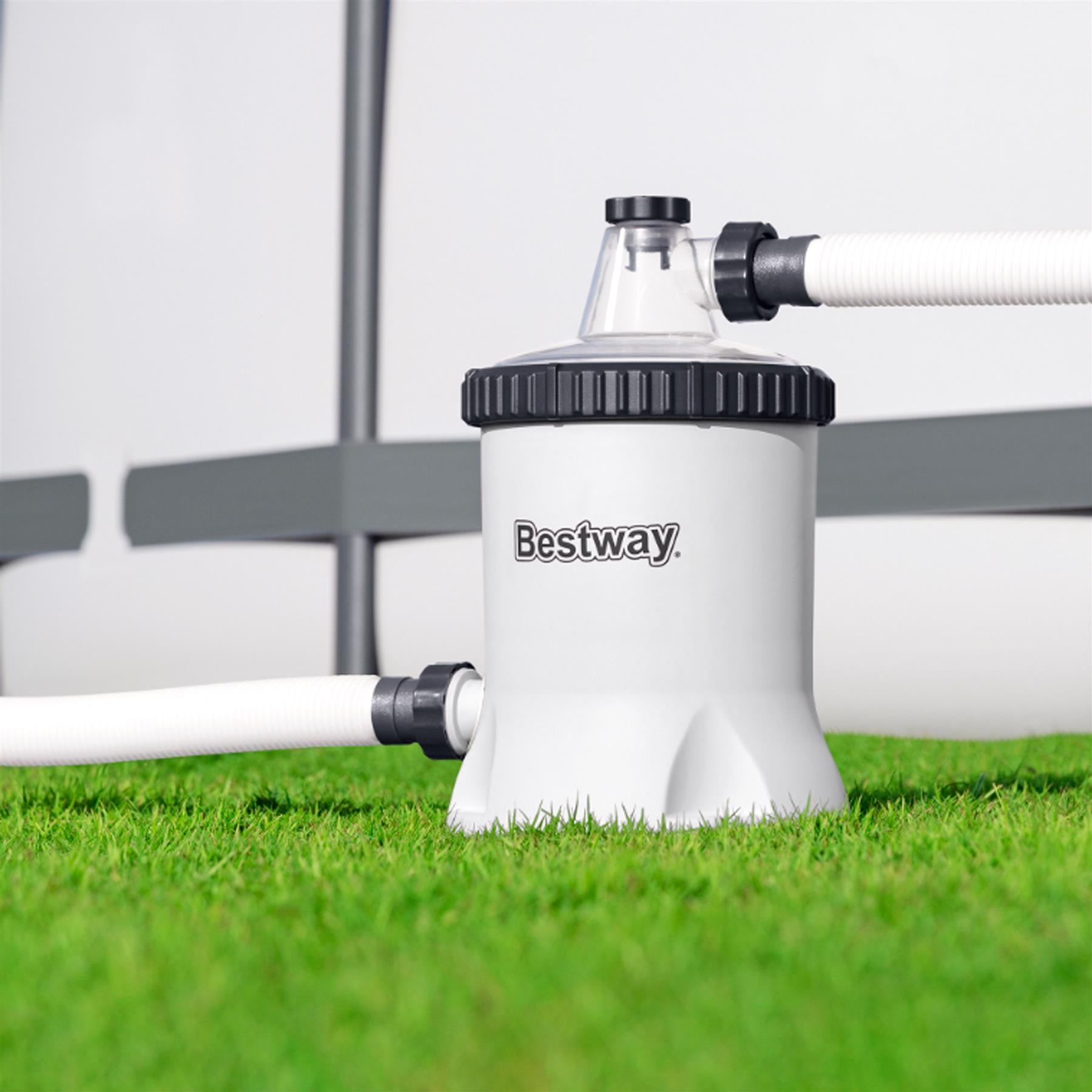 White pool filter pump housing sits on green grass with white hoses connected.