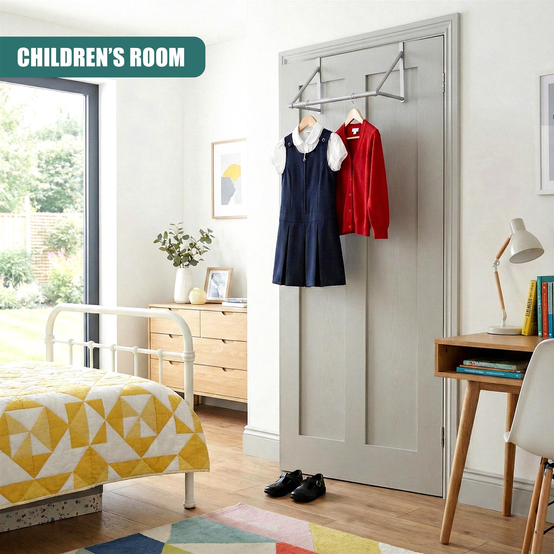 A children's bedroom with a bed, desk, and wardrobe. The room features a white bed with a yellow and white quilted cover, a desk with a white chair, and a wardrobe with a hanging rail. A child's wardrobe is hung with a blue dress and a red cardigan, and a pair of black shoes is on the floor. The room is bright and well-lit, with a window to the left of the bed. - The Magic Toy Shop