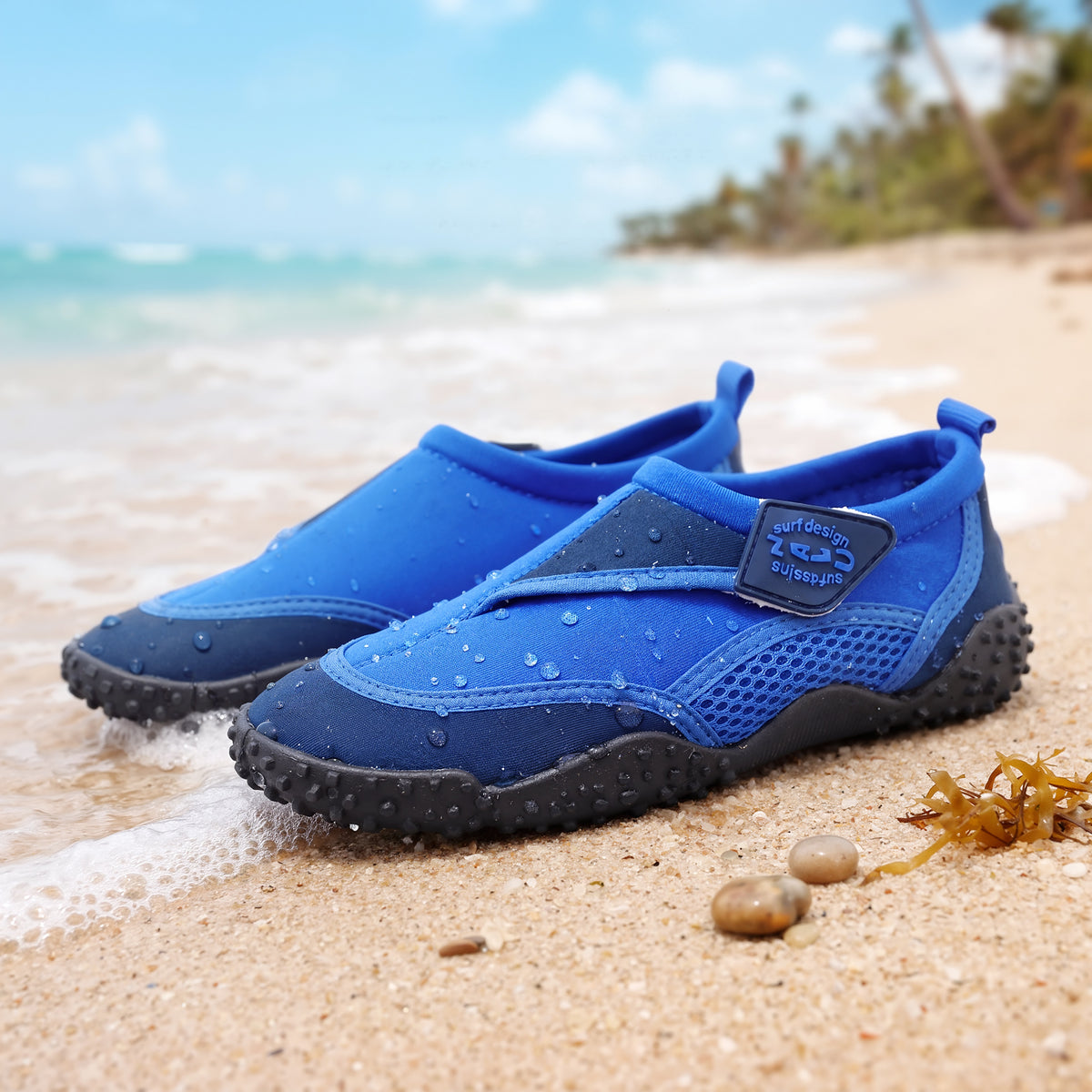 Blue GEEZY aqua shoes on a sandy beach, ready for seaside adventures