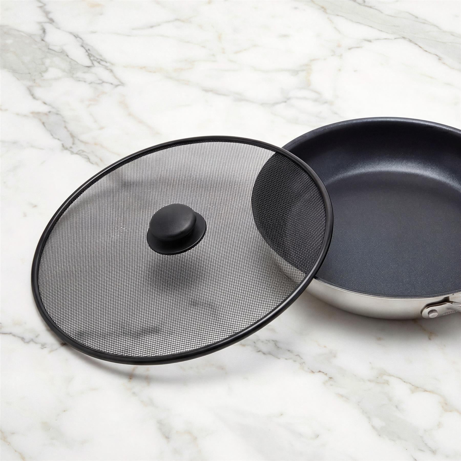 Black mesh splatter screen and dark frying pan arranged on a white marble surface.