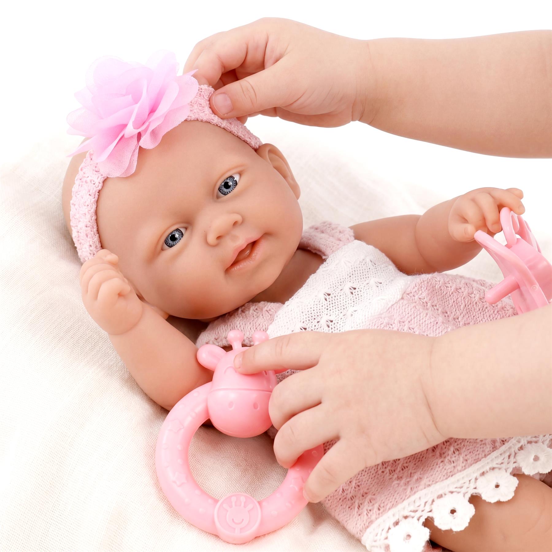 Adult hands adjust the doll's pink floral headband and hold a circular pink rattle toy.