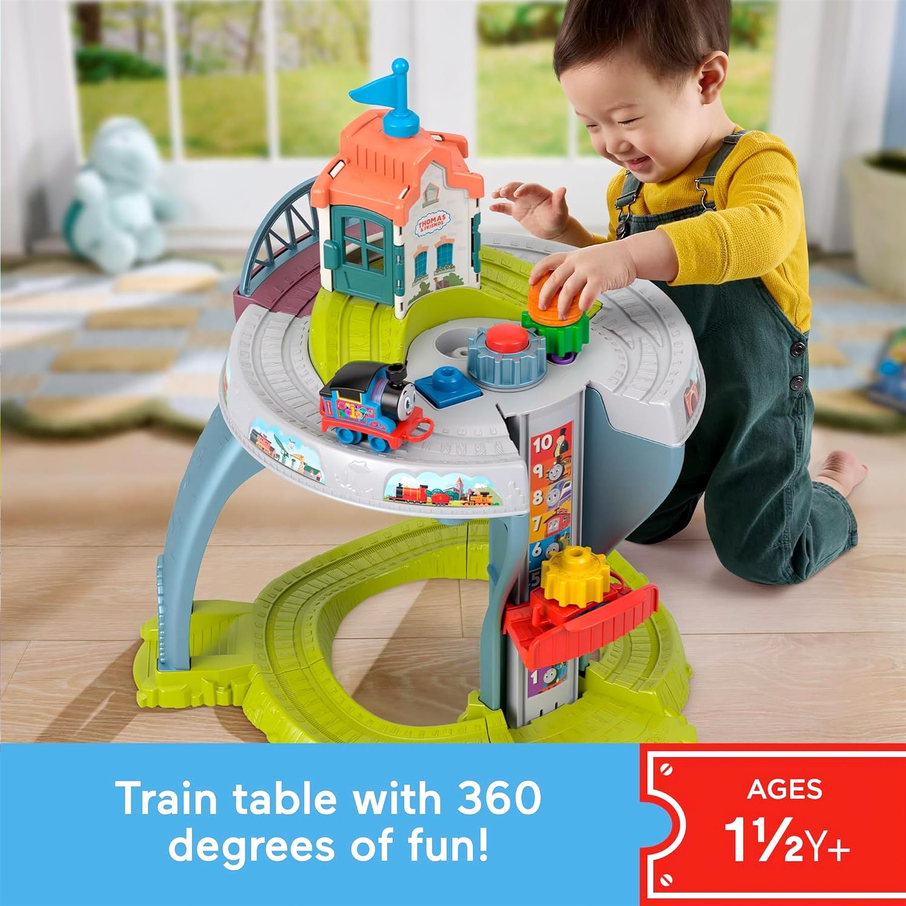 Child interacting with a multi-level train table set, featuring tracks and a small house structure.