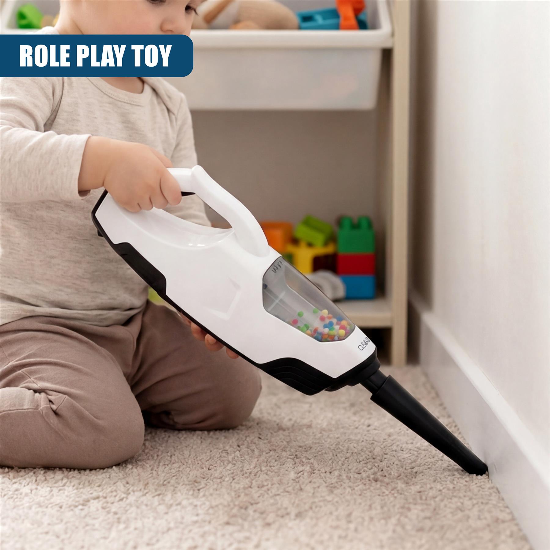 A child plays with a white and black toy vacuum cleaner on a light colored carpeted floor.