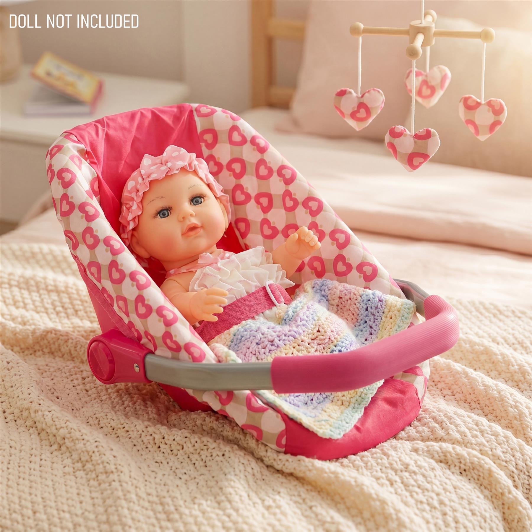 Pink baby doll car seat with a pink patterned lining, containing a baby doll and blanket.