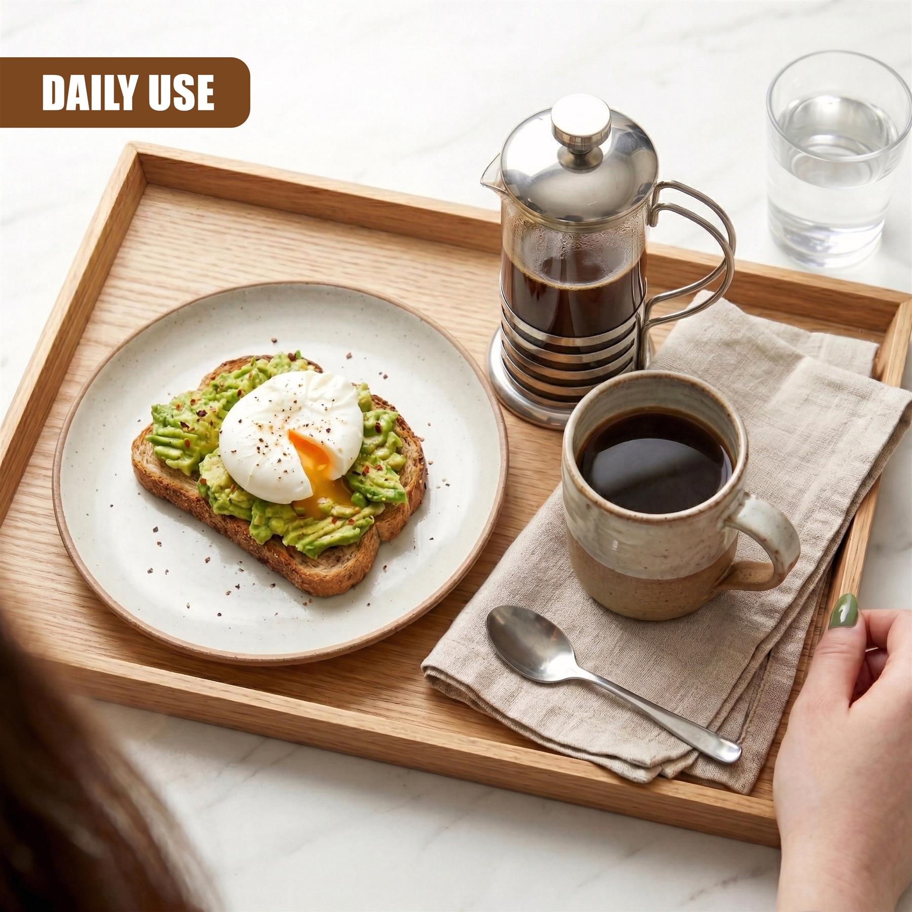 Silver cafetiere carafe on a wooden serving tray, next to coffee and avocado toast.