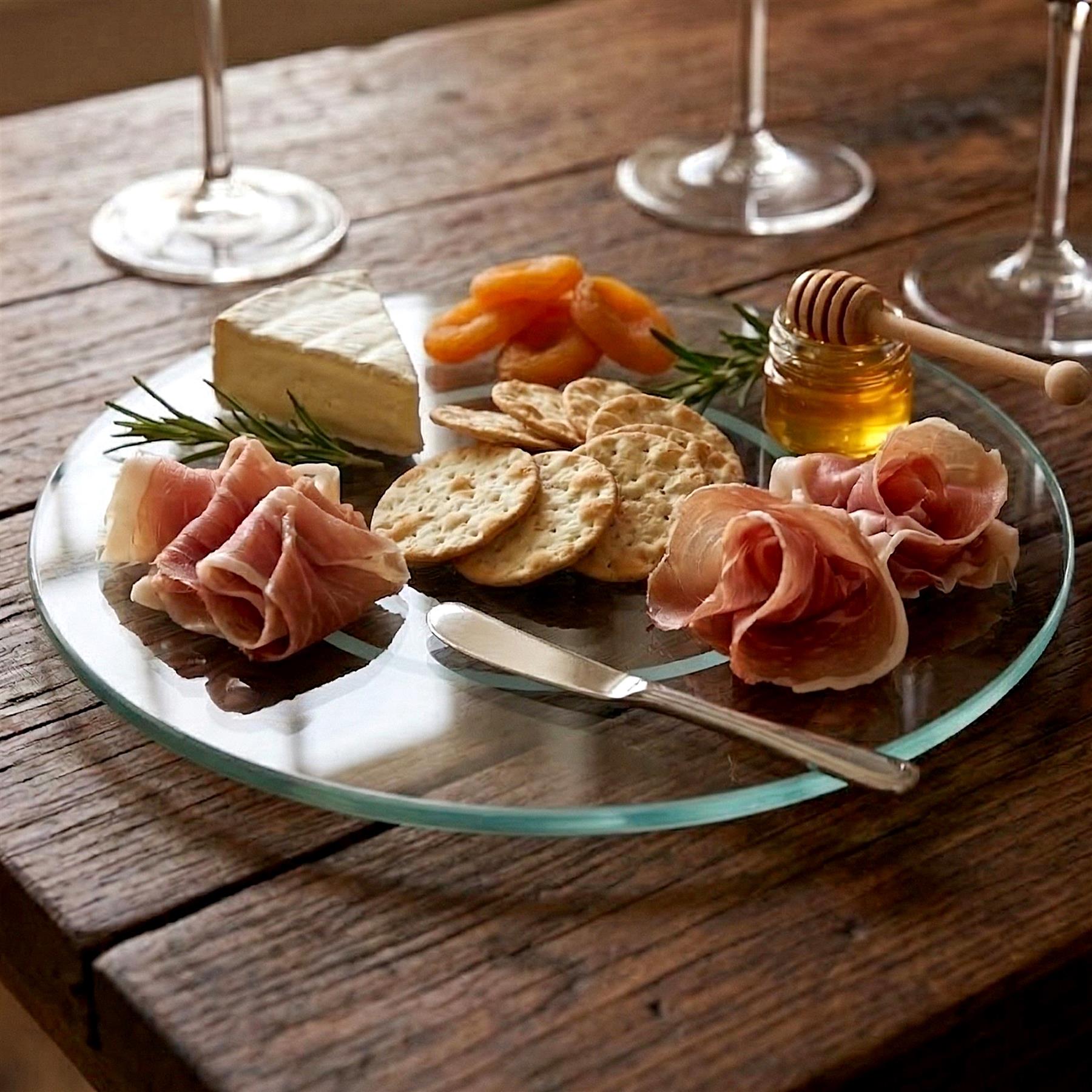 Glass turntable presenting charcuterie, cheese, crackers, honey, and fresh fruit samples.