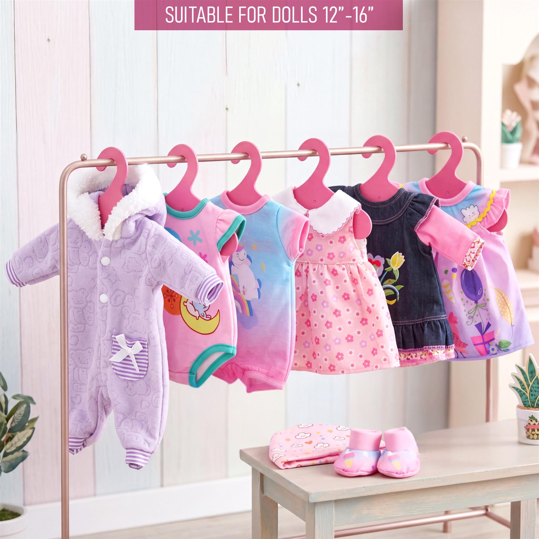 A set of six patterned and solid doll clothes are displayed hanging on a pink clothes rack.