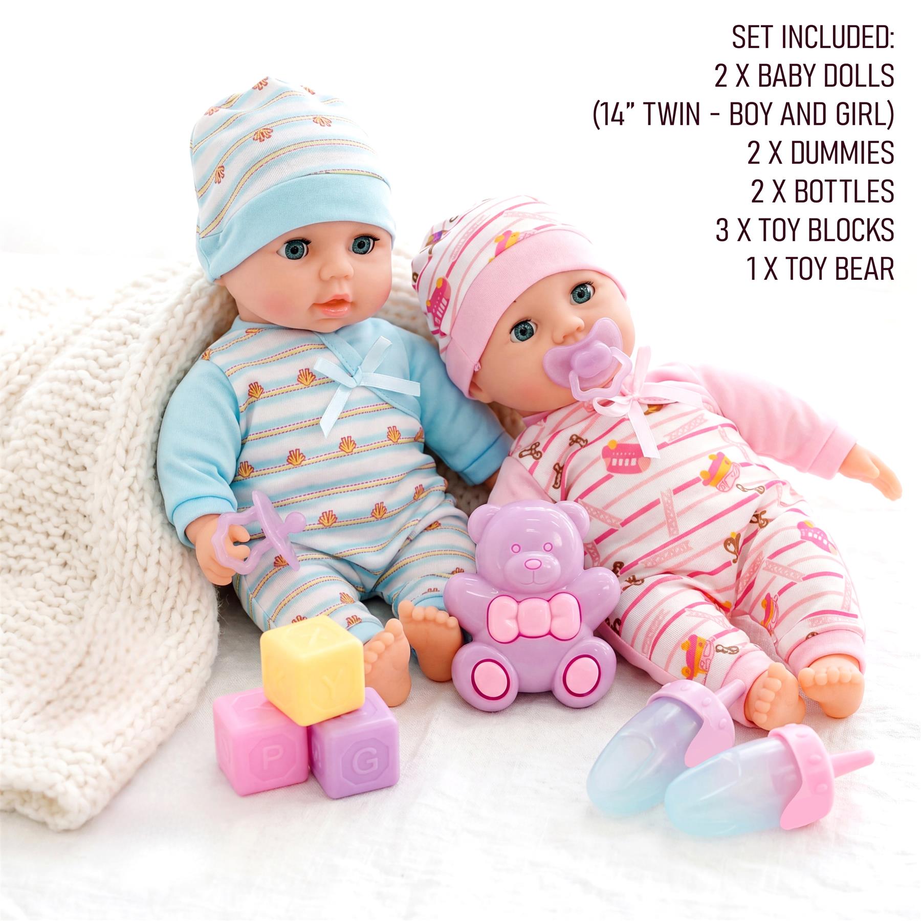 Twin dolls sit with blocks, bottles, a bear toy, and a knitted blanket accessory.