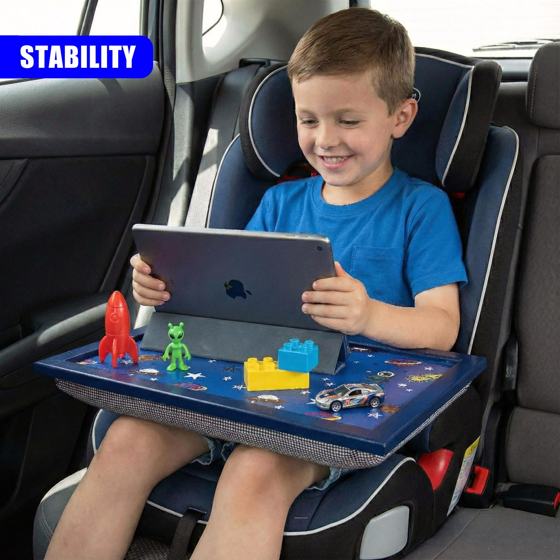 Boy uses a blue lap tray attached to a car seat while playing with toys and a tablet.