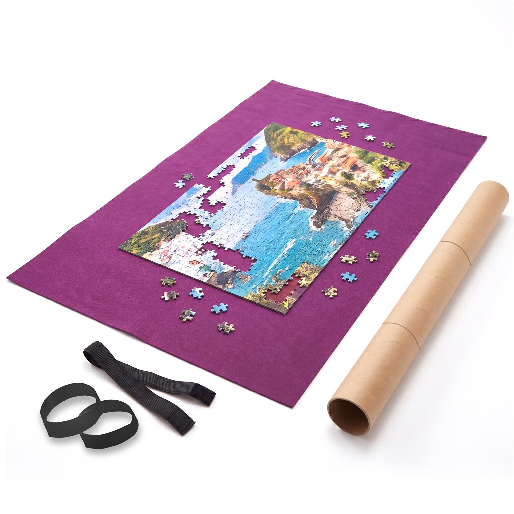 Purple mat displaying a coastal puzzle, scattered pieces, black ribbon, and rolled cardboard tube.