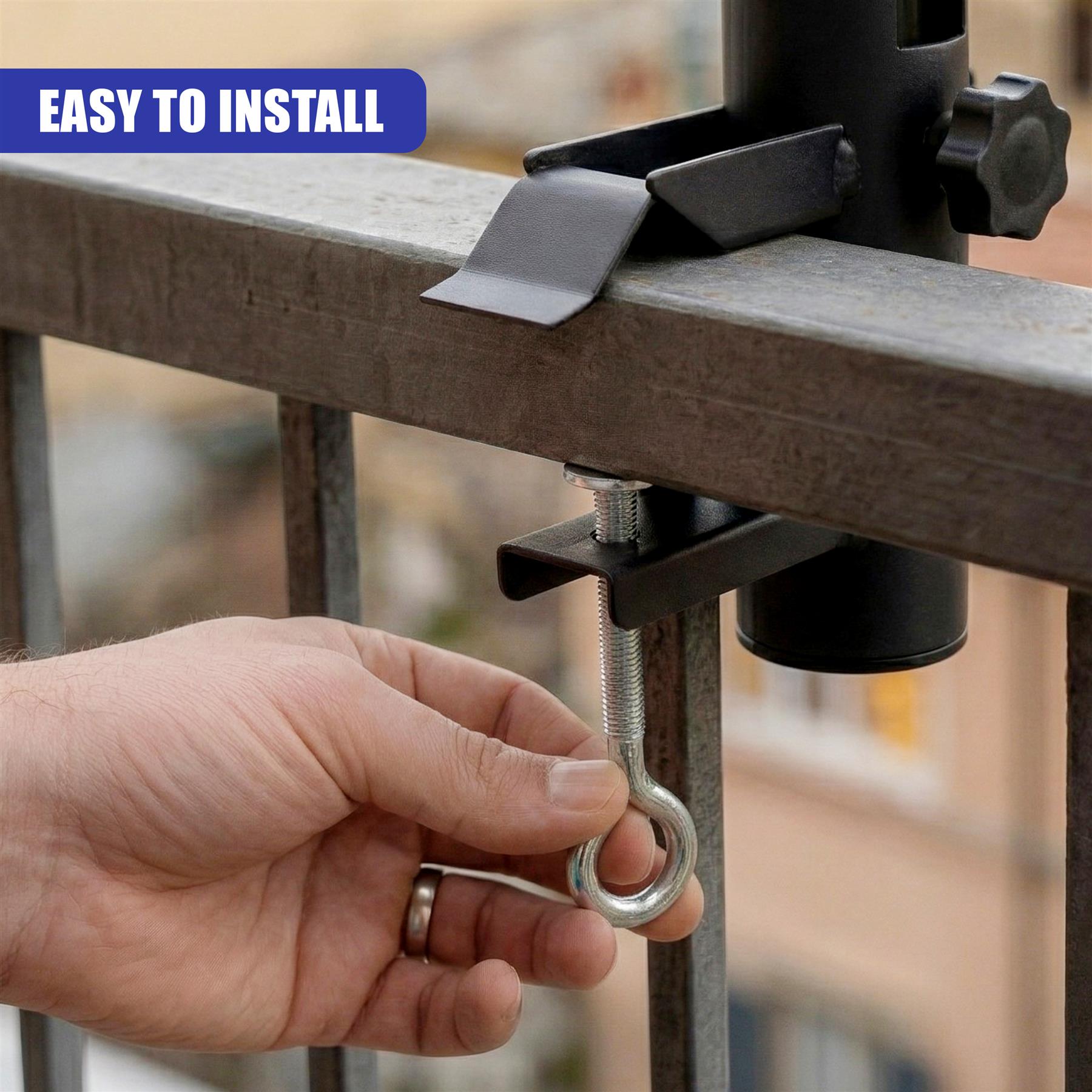 A hand holds a U-hook attached to a metal clamp mechanism gripping a dark railing.