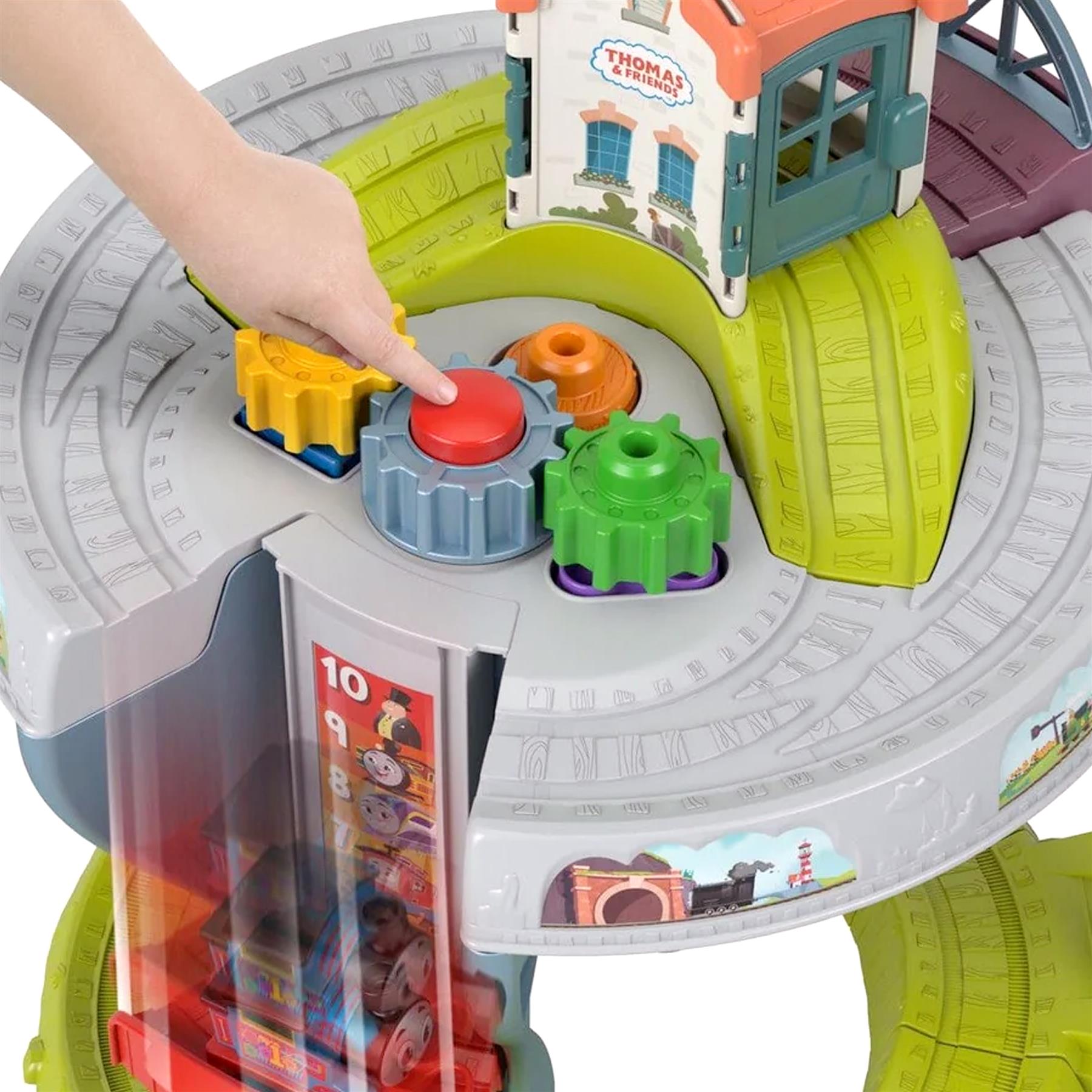 A hand places colorful gear attachments on the track near a light blue train house structure.