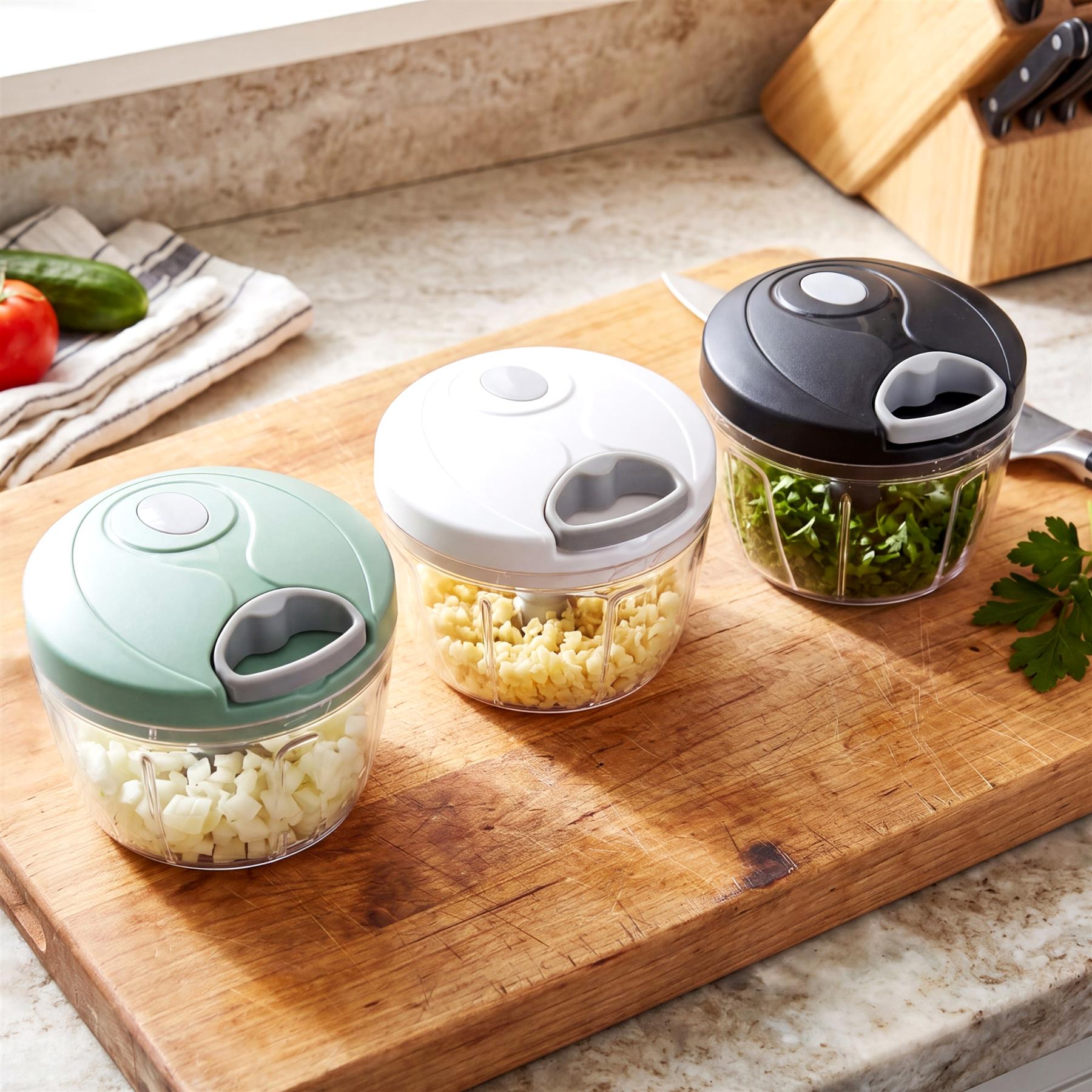Three manual food choppers with lids filled with chopped ingredients sit on a wooden cutting board.