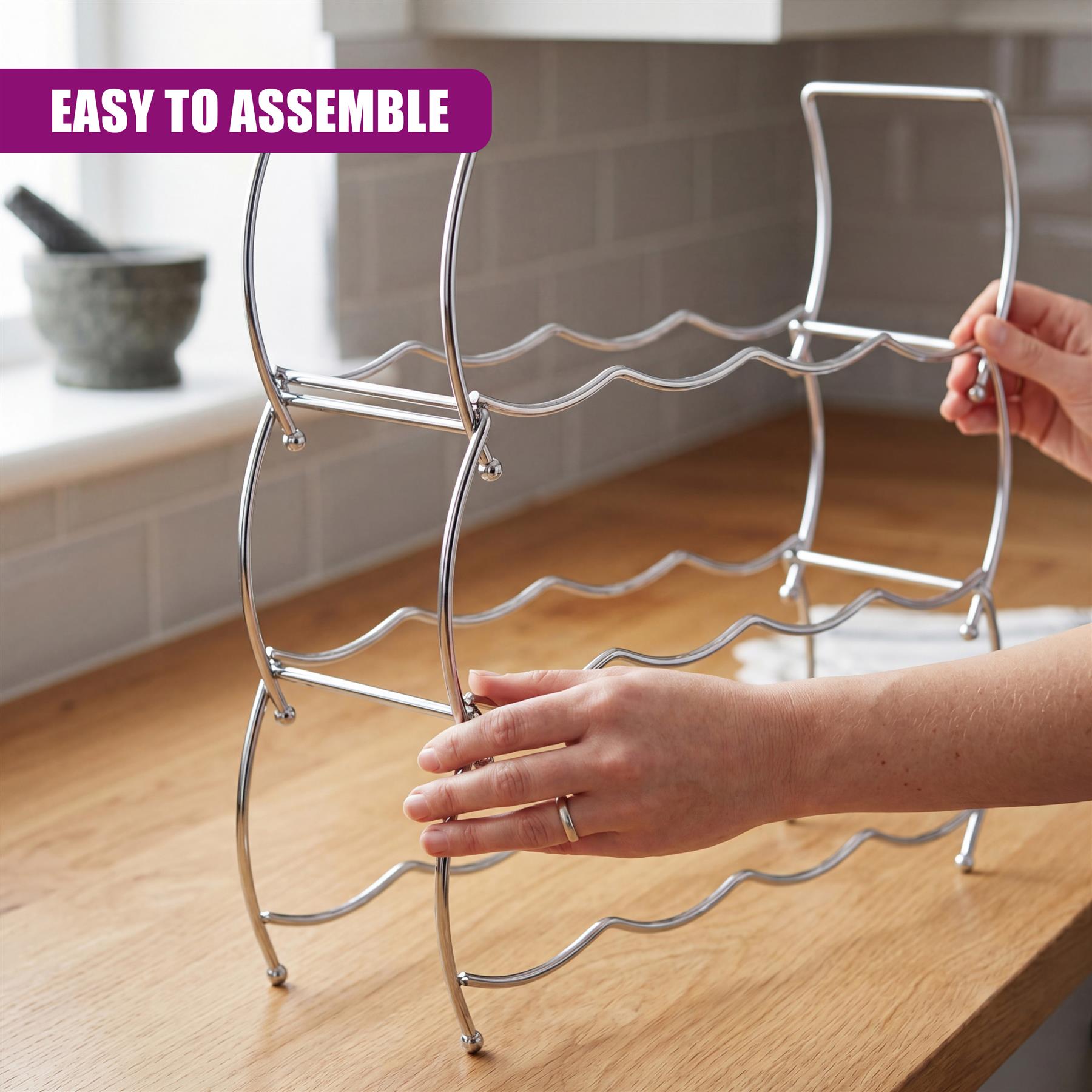 A person's hands hold a tiered silver metal wine rack on a light wooden countertop.
