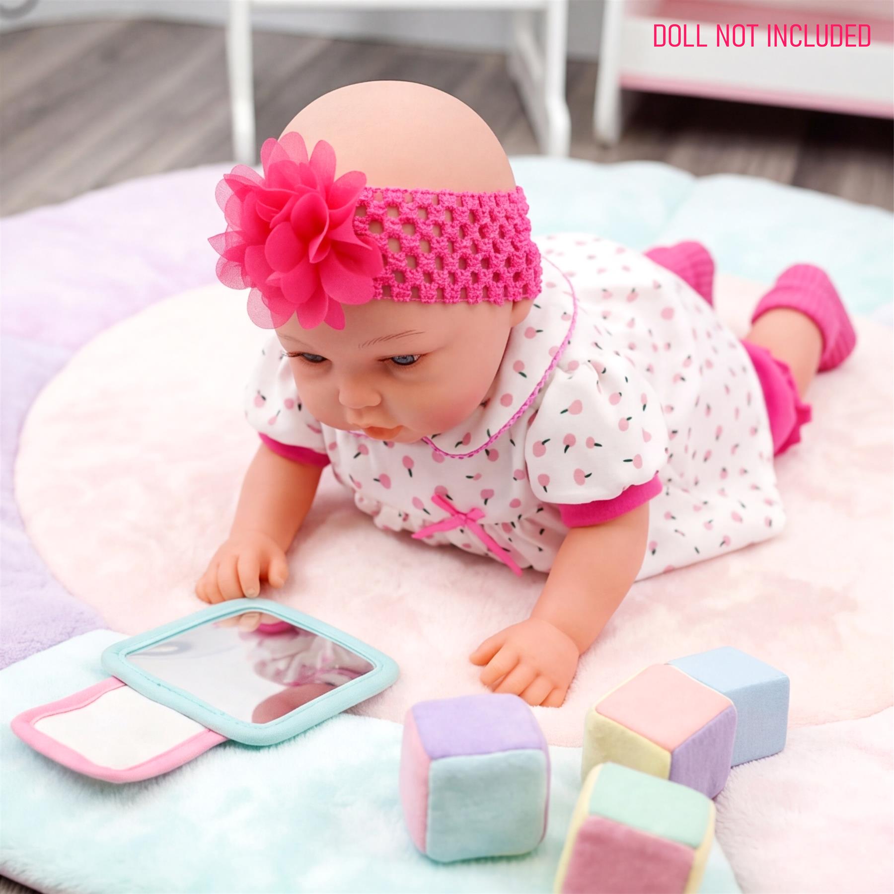 Reborn doll with pink outfit rests on a blanket with a mirror and pastel square blocks.