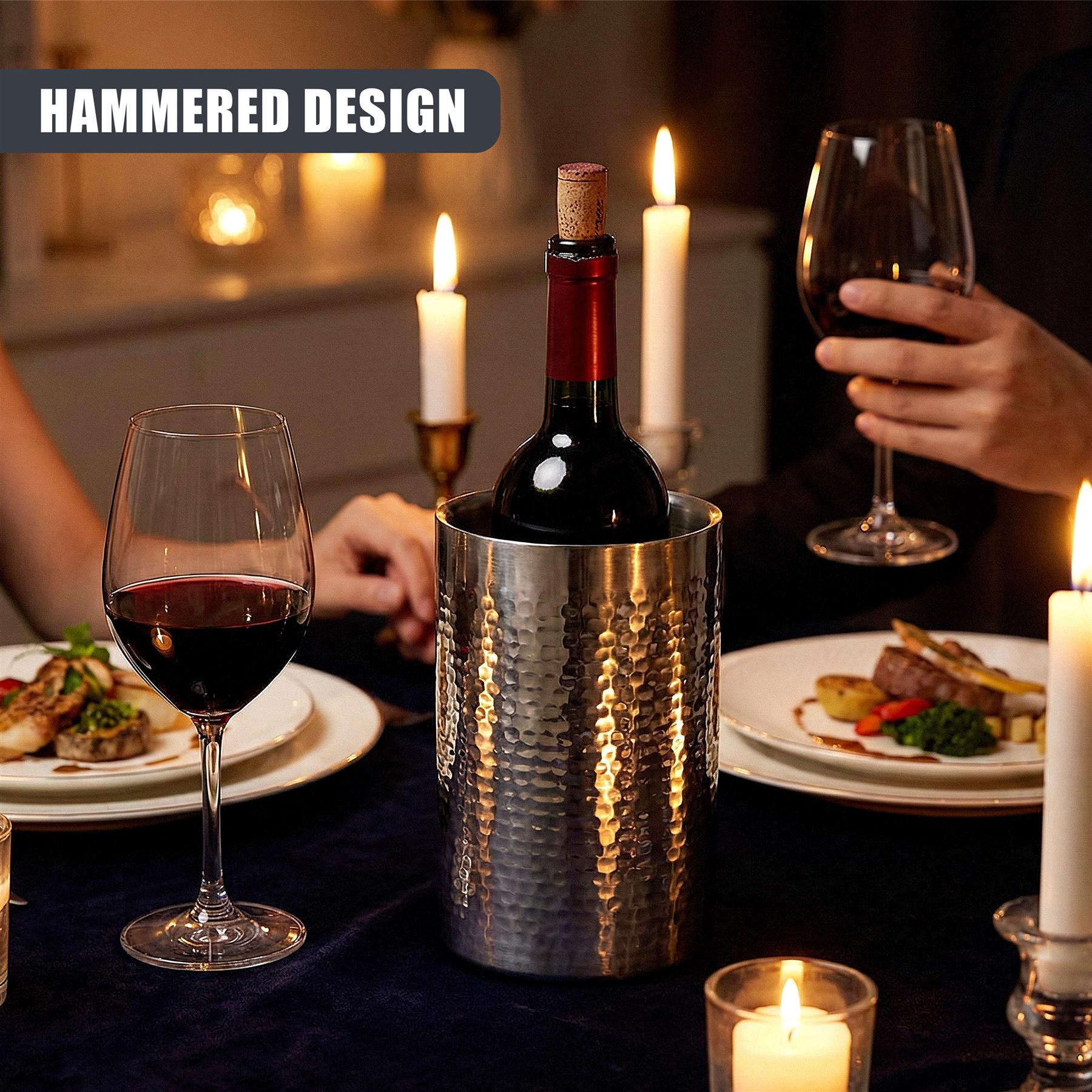 Wine glasses and plates surround a hammered stainless steel wine cooler holding a dark bottle.