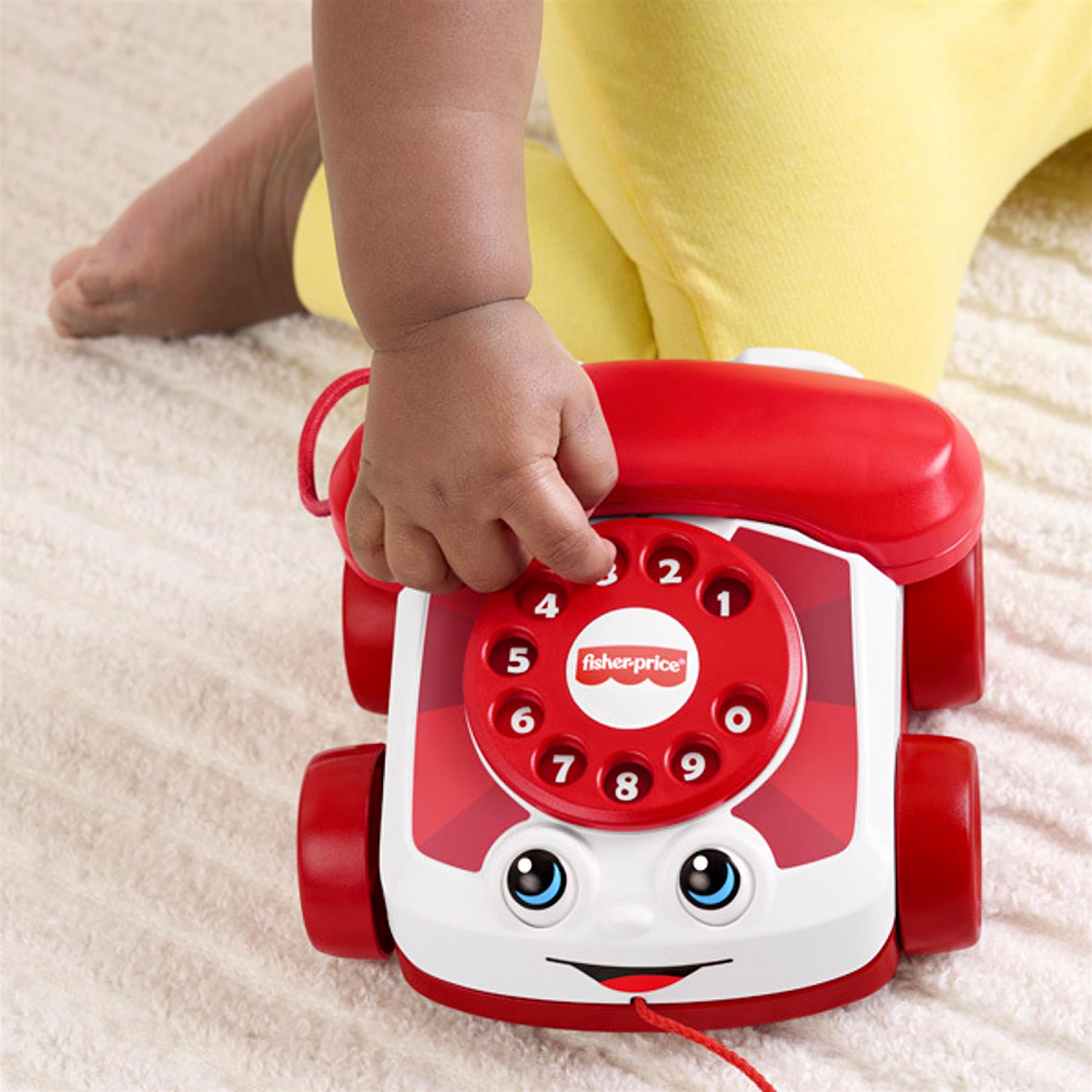 Red Fisher-Price telephone toy with a keypad, being pressed by a small child's finger.