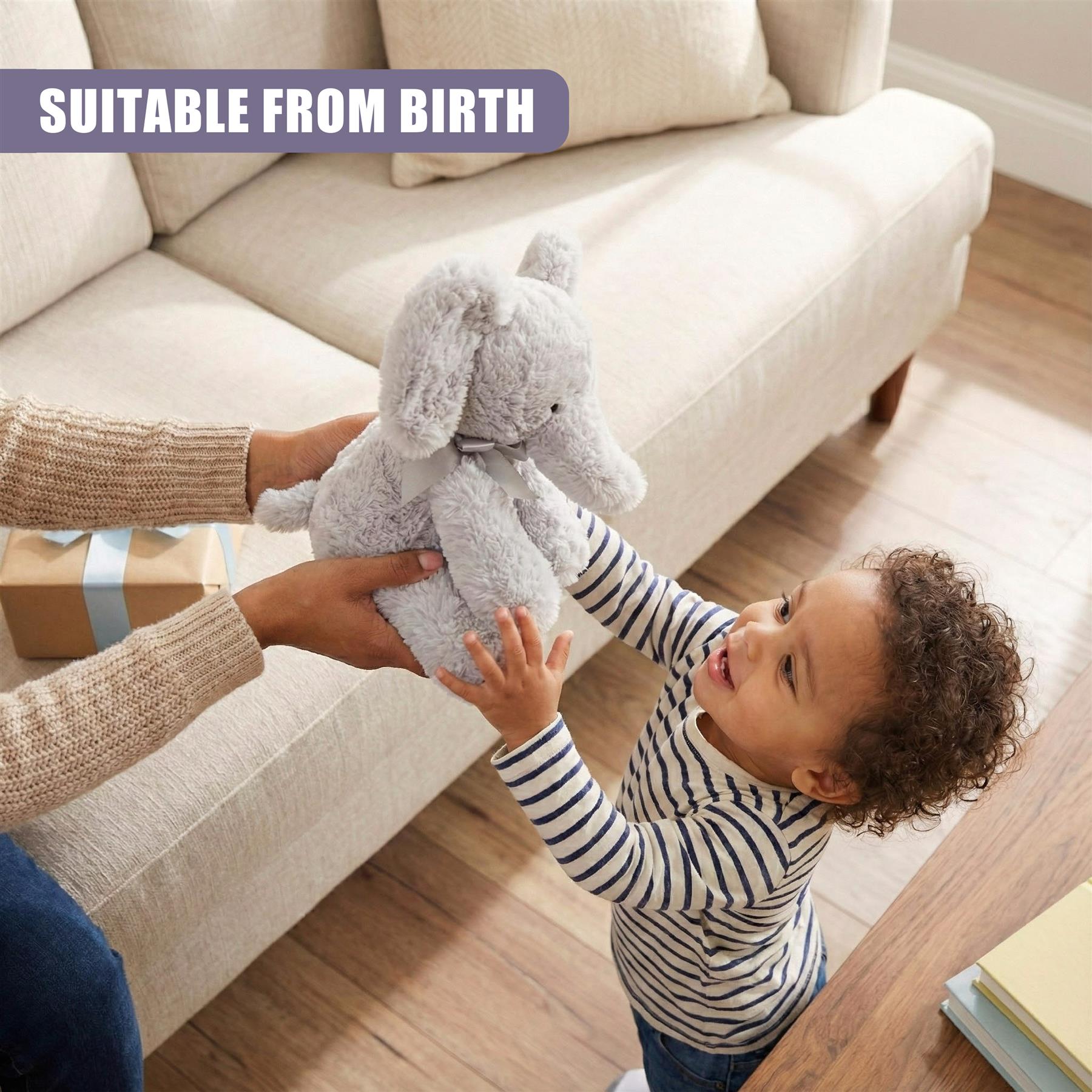A child holds a plush toy elephant, with a gift box and a couch in the background. The child's hand is being guided by an adult, with the adult's arm and hand visible in the frame. - The Magic Toy Shop