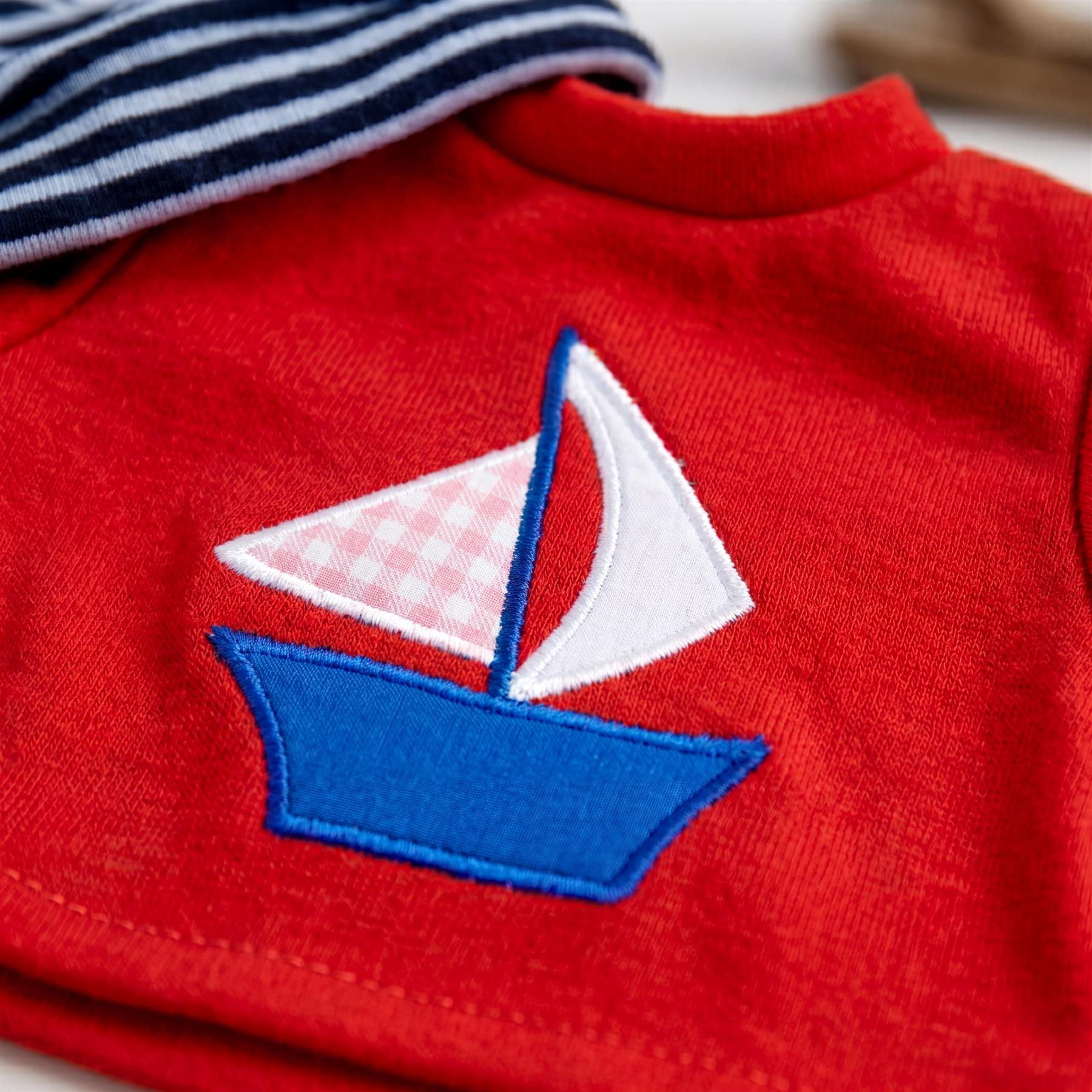 Red knit top featuring a stylized blue and white embroidered sailboat appliqué on the chest.
