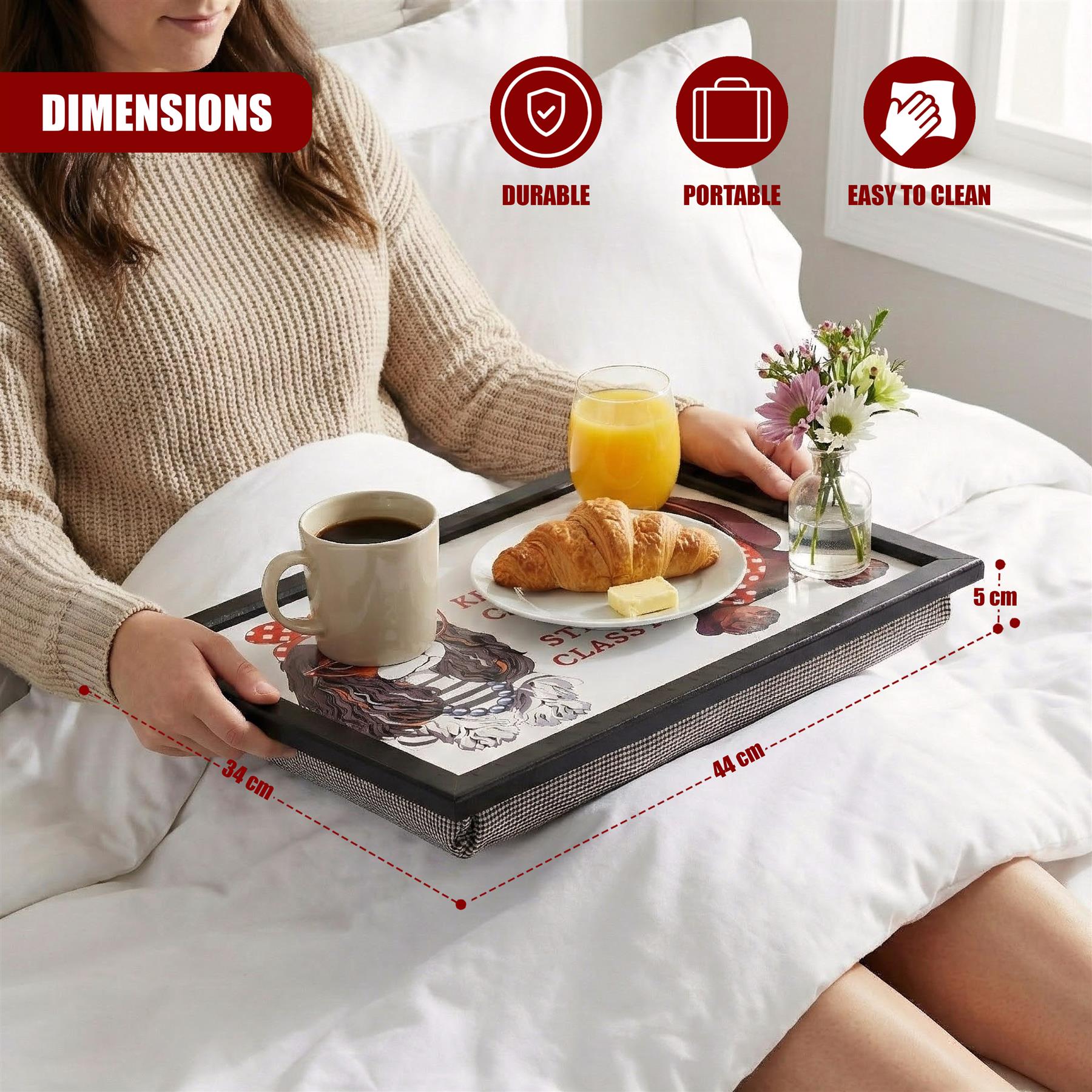 Black lap tray on a bed holds a coffee cup, croissant, orange juice, and vase of flowers.