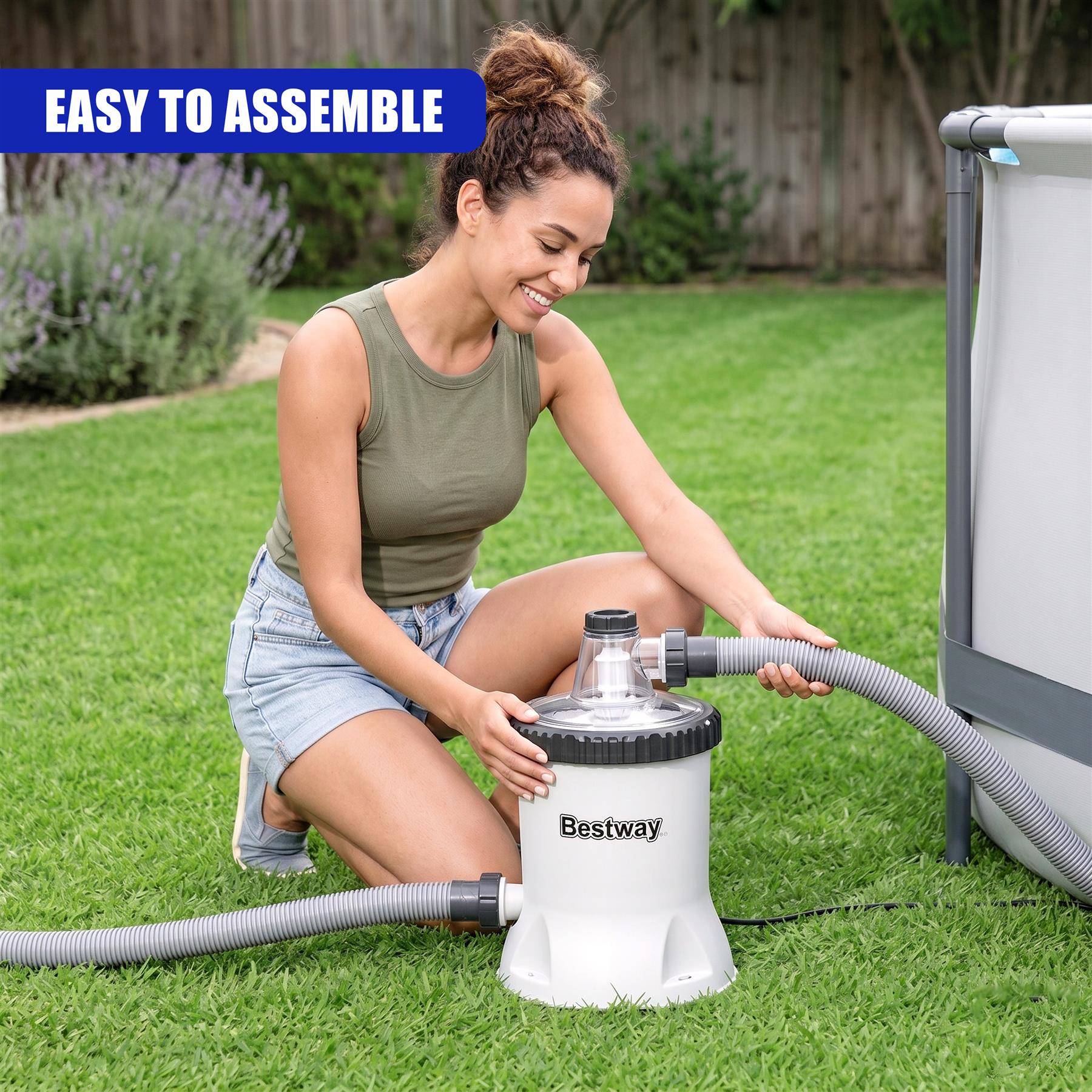 Woman assembling a white Bestway pool filter pump unit and hoses on a green lawn.