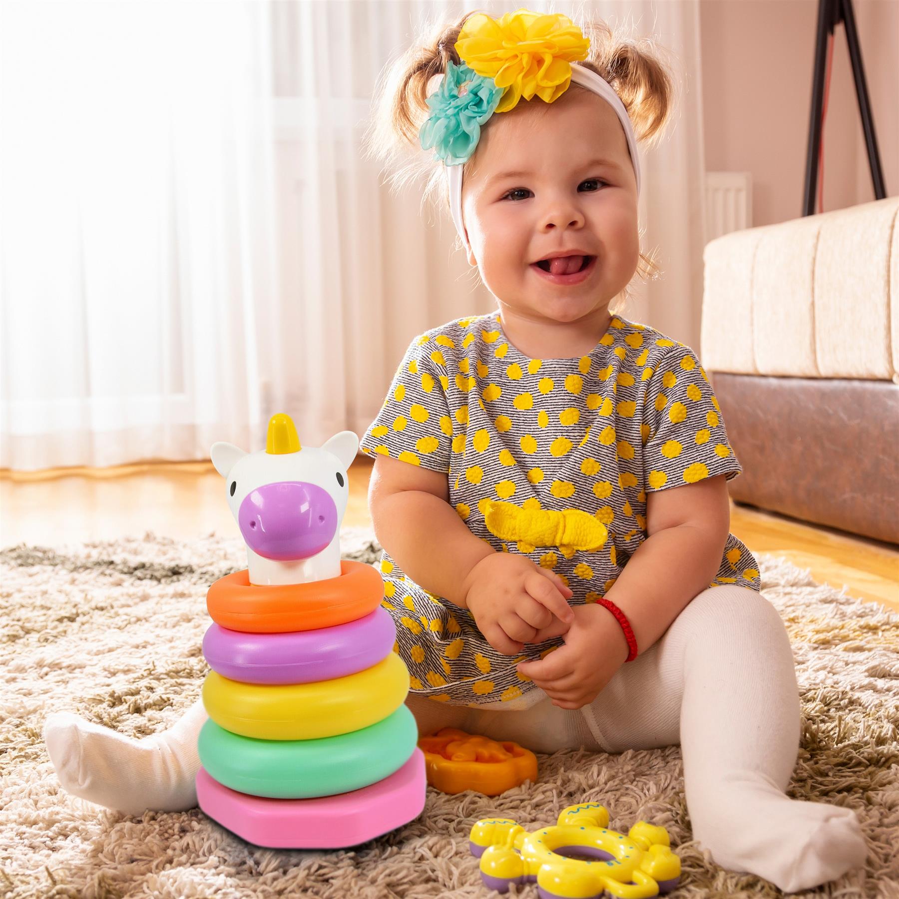 Smiling girl plays with a multi-colored giraffe stacking rings toy set on a plush rug.