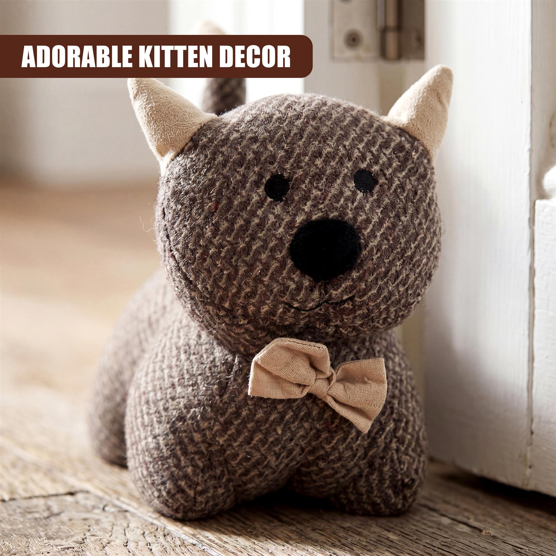 Crocheted grey kitten door stopper with a bow, resting on a wooden surface by a doorway.