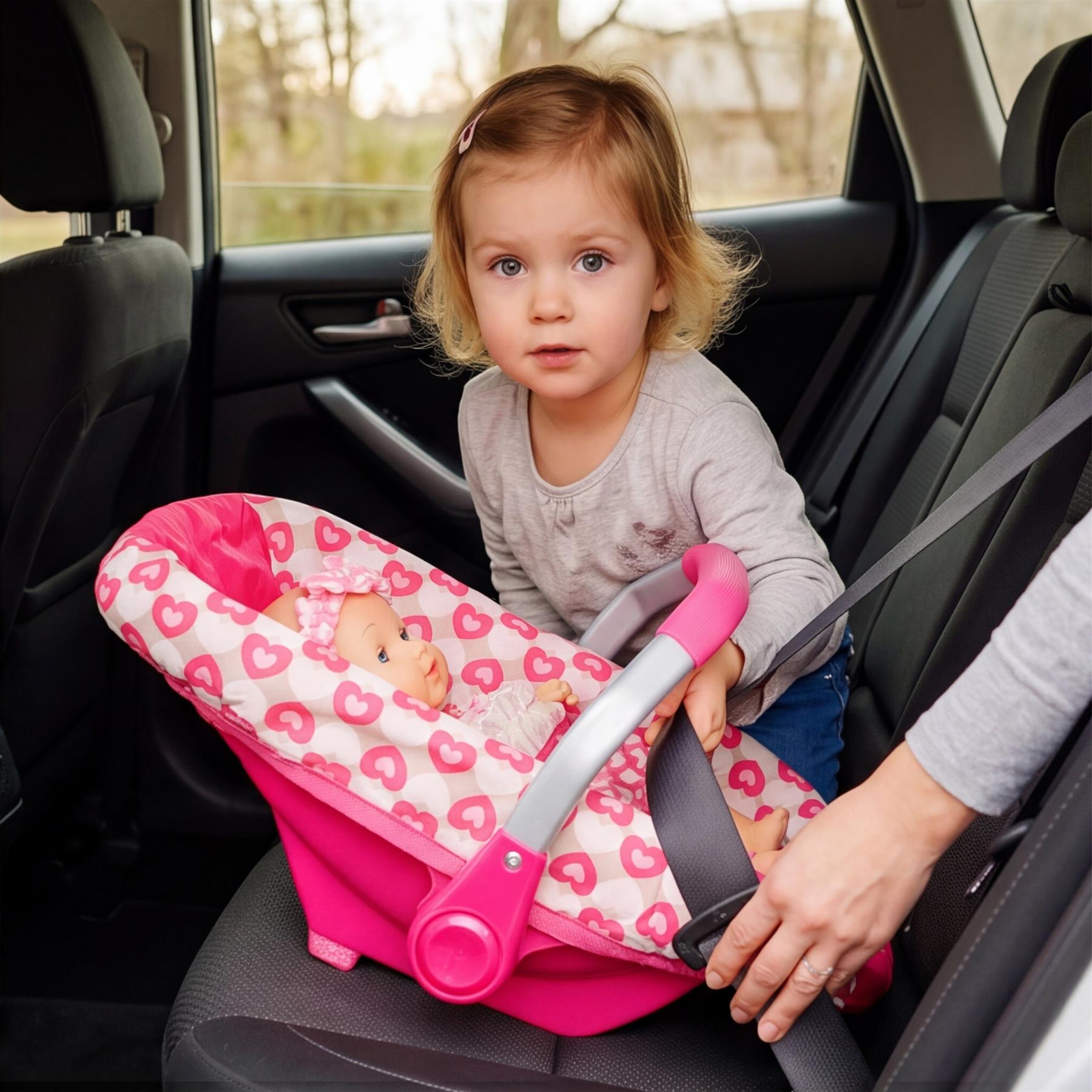 Pink patterned baby car seat installed in a vehicle, containing an infant with an older girl visible.