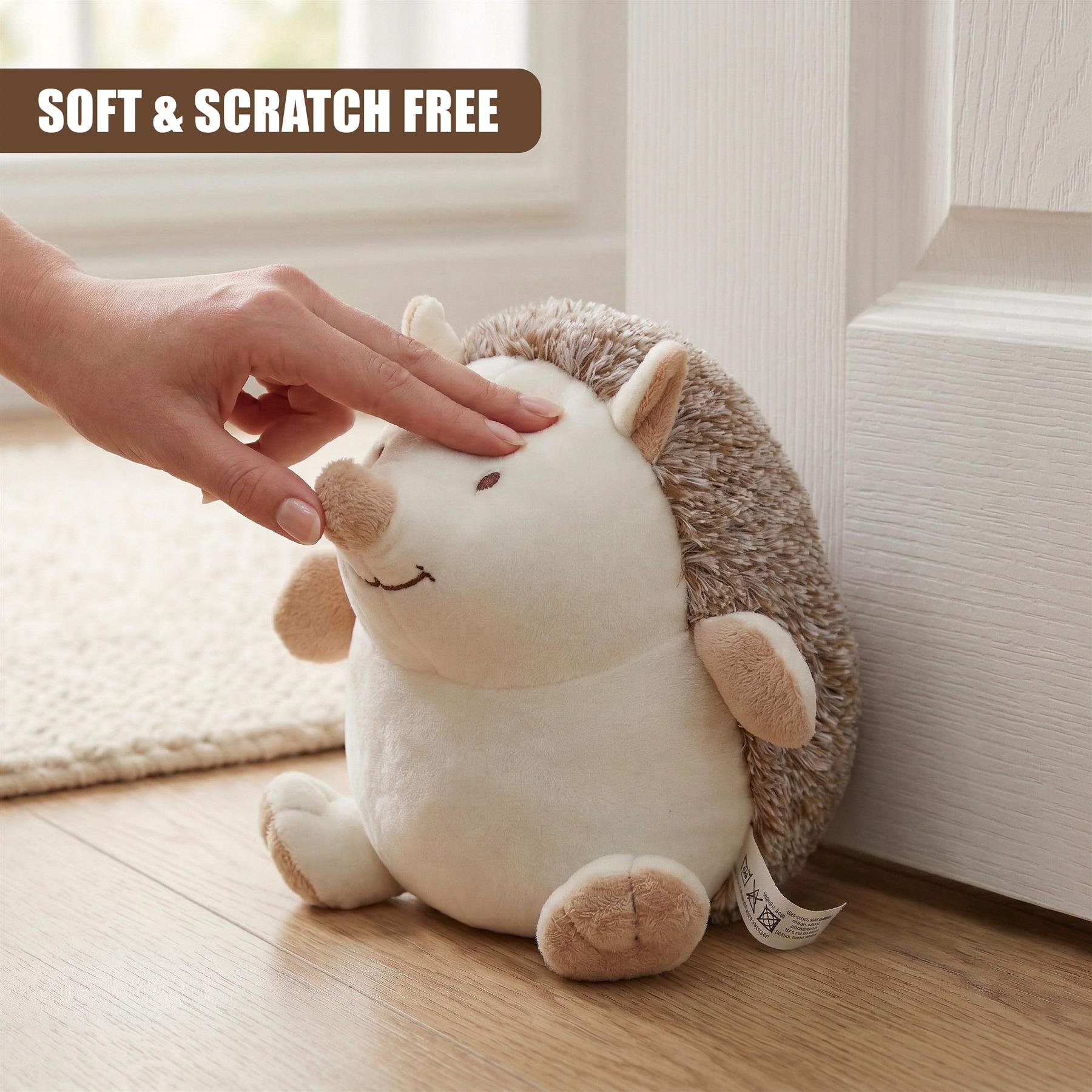 A human hand gently touches a plush hedgehog door stopper resting on a hardwood floor.
