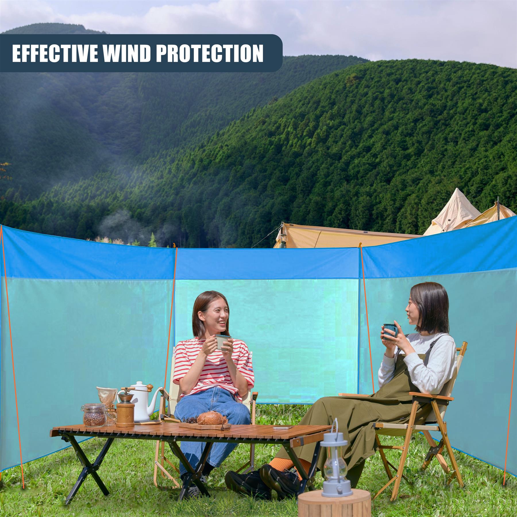 Two women sit at a picnic table under a canopy tent overlooking lush, forested mountains.