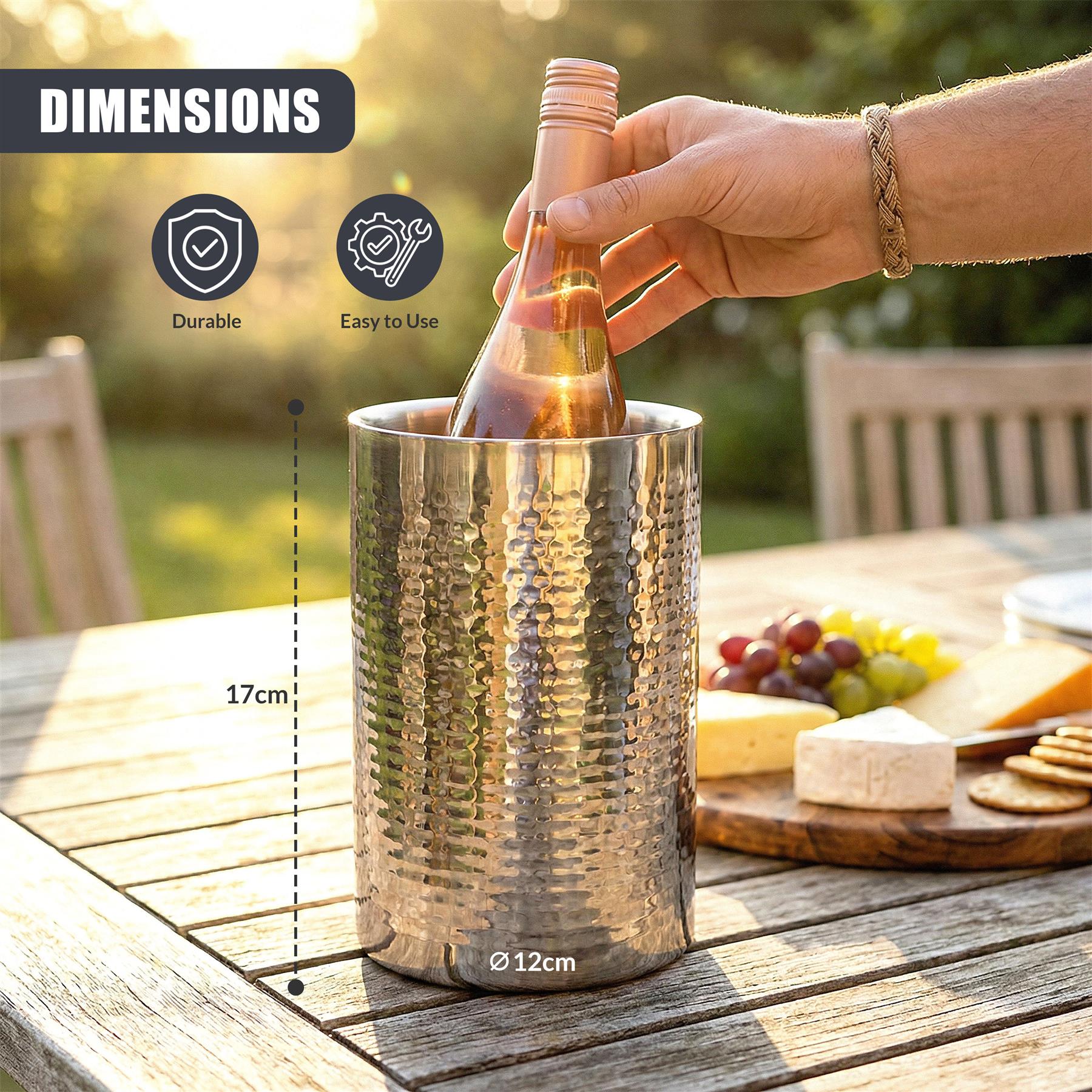 Hammered stainless steel wine cooler holding a bottle on a rustic wooden table next to snacks.