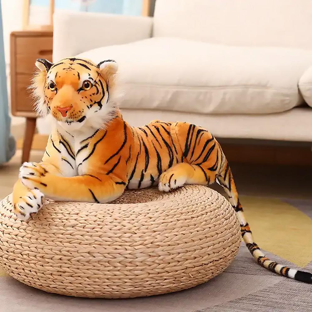 Plush Bengal tiger toy placed on a woven circular pouf against a modern couch.