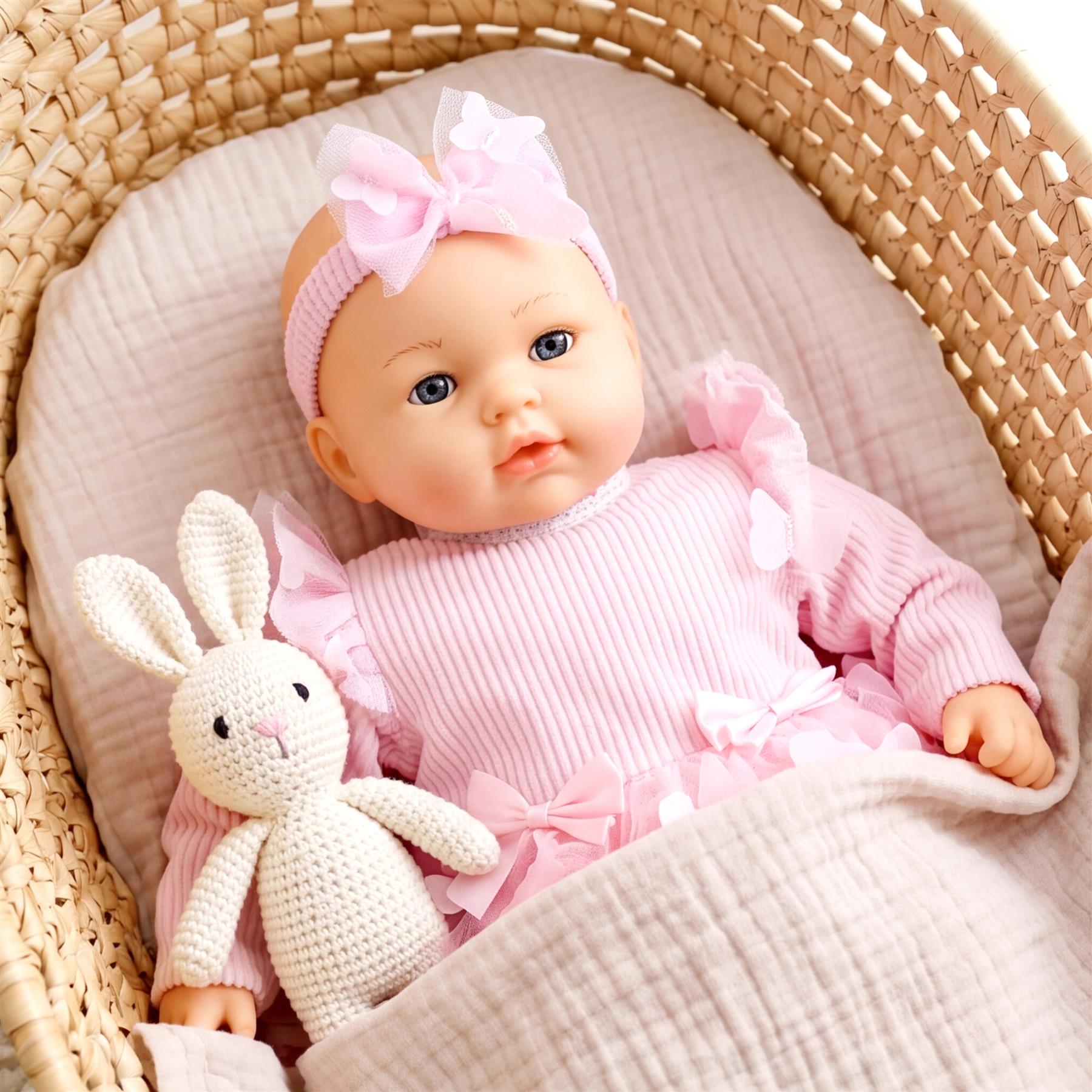 Doll in a woven basket, wearing a pink outfit and bow, rests next to a crocheted white bunny toy.