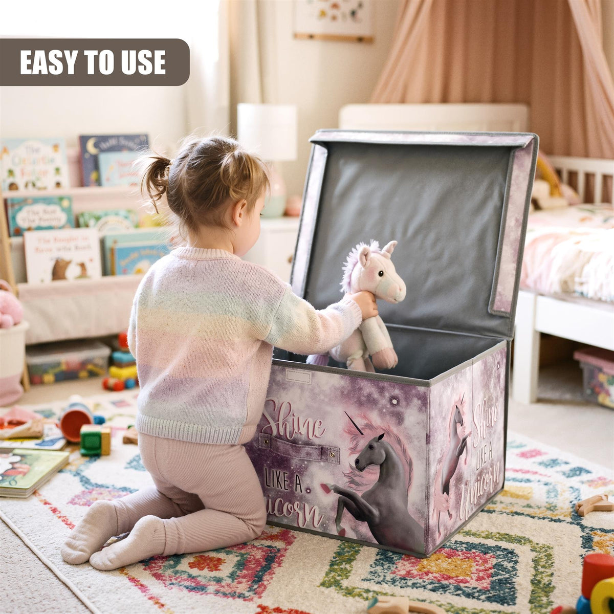 A young girl kneels beside a large, purple unicorn storage box with a plush unicorn toy