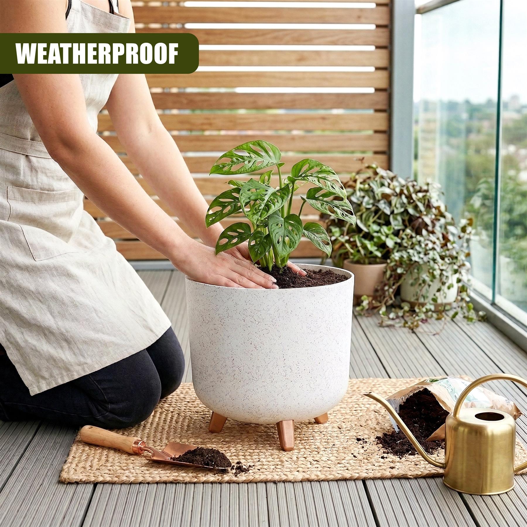Person pots a green plant into a white, three-legged ceramic flower pot resting on a woven mat.