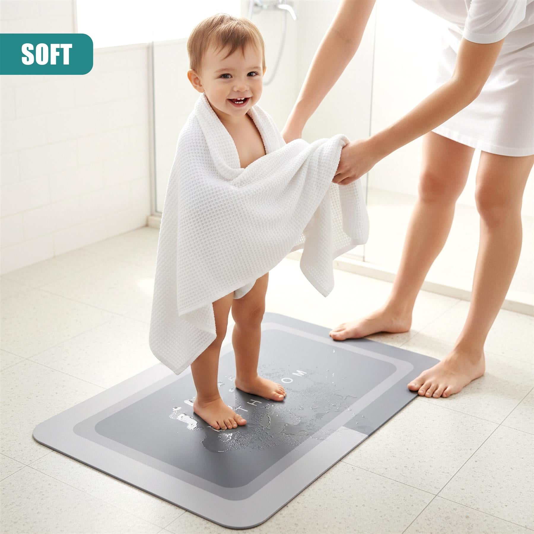 A child stands on a rectangular grey bath mat, wrapped in a towel, near an adult.