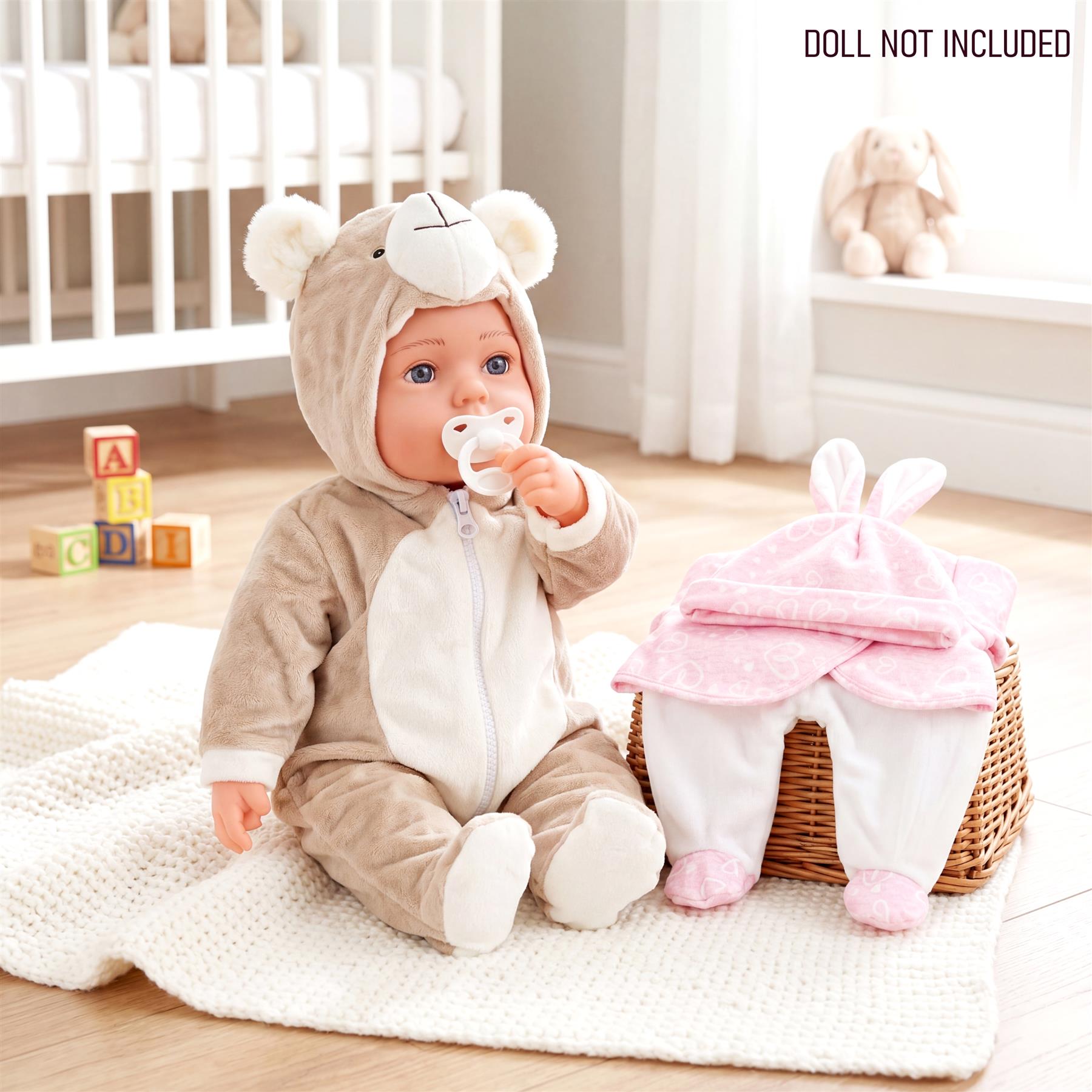 Doll dressed as a bear sits beside a basket containing a pink and white bunny outfit.
