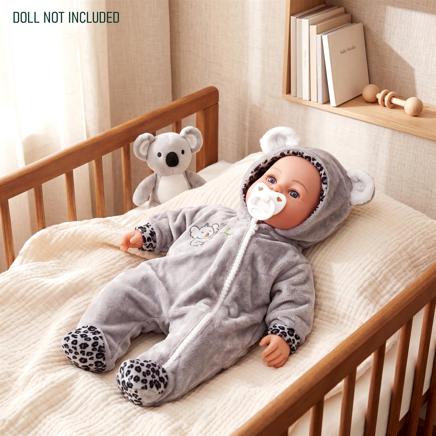 Gray knitted doll outfit with hood and spots, displayed on a crib mattress beside a stuffed animal.