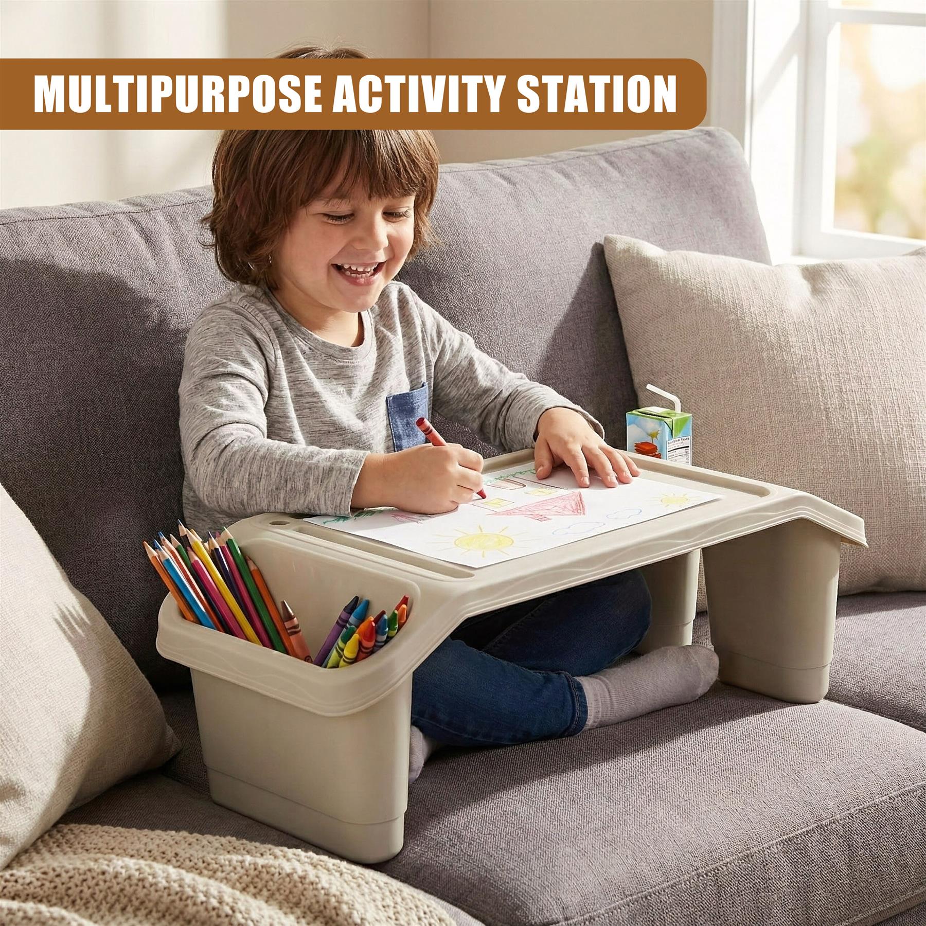 A child sits on a couch, using a lap desk with a tray and storage container. The desk has a built-in cup holder and a compartment for holding art supplies. The child is drawing on a piece of paper, using a crayon. - The Magic Toy Shop